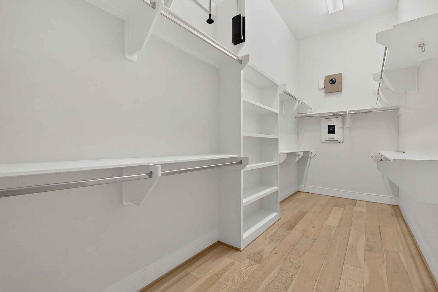 Spacious walk-in closet with ample shelving and hanging space, featuring sleek white finishes and light hardwood floors for a modern touch.