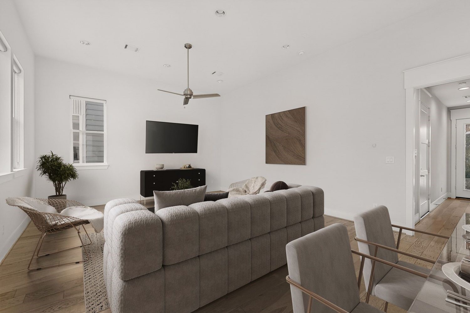 Spacious and modern living room featuring an area fora  sectional sofa, sleek ceiling fan, mounted TV, and abundant natural light from large windows.