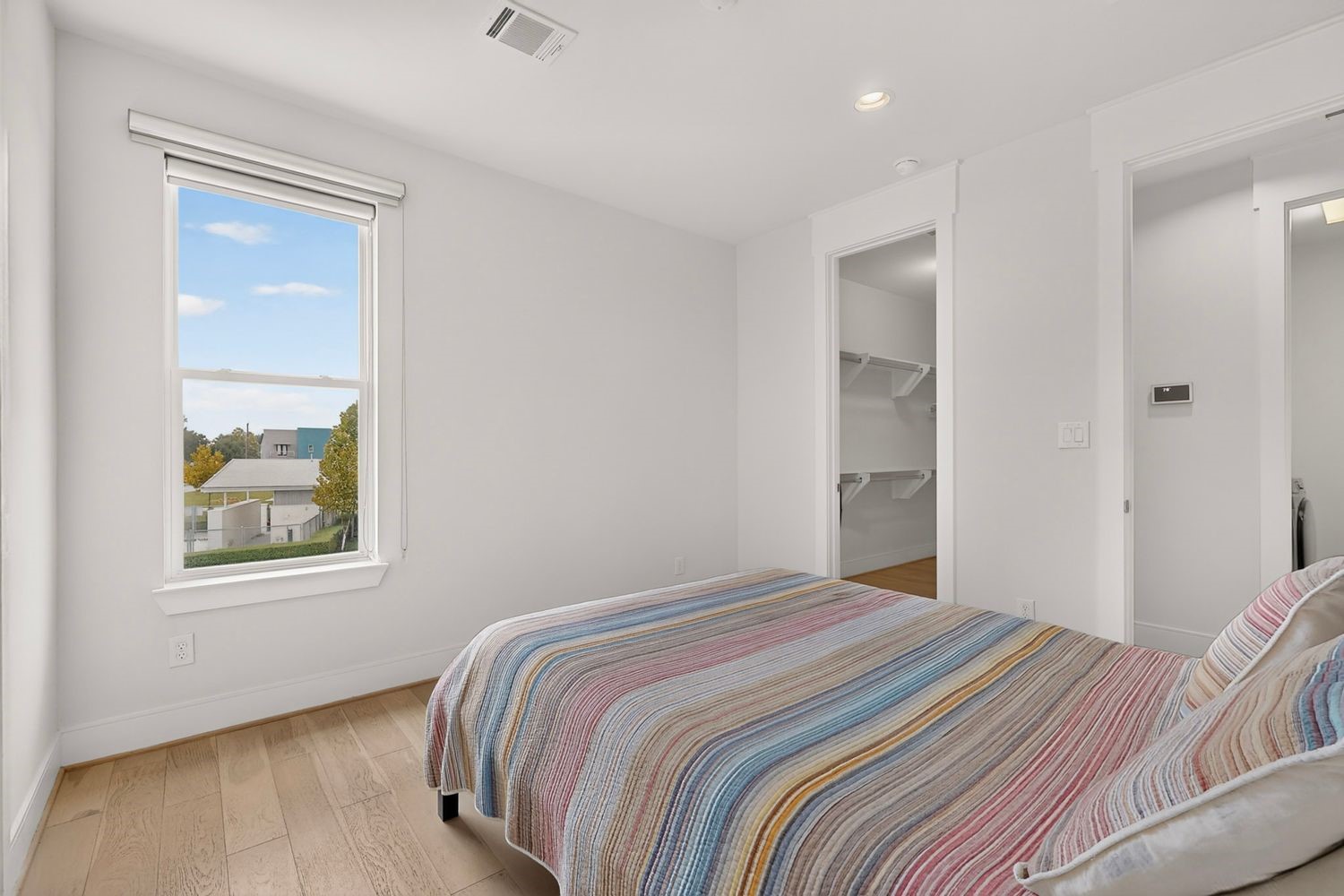 Bright and inviting bedroom featuring a large window with scenic views, hardwood floors, and access to a spacious walk-in closet.