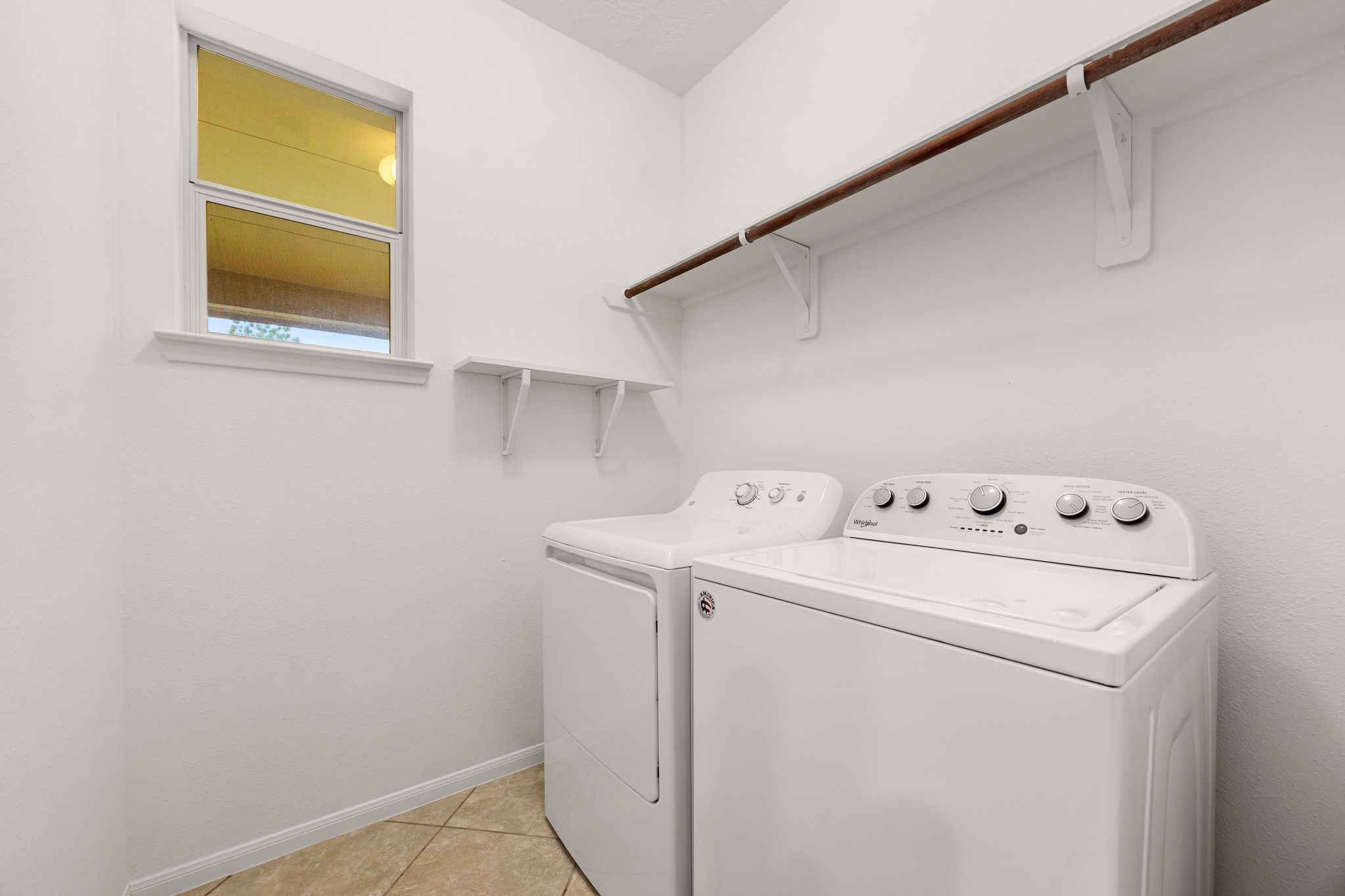 The utility room keeps chores simple, with electric dryer and washer connections, a built-in shelf, a hanging rod, and a window for natural light.