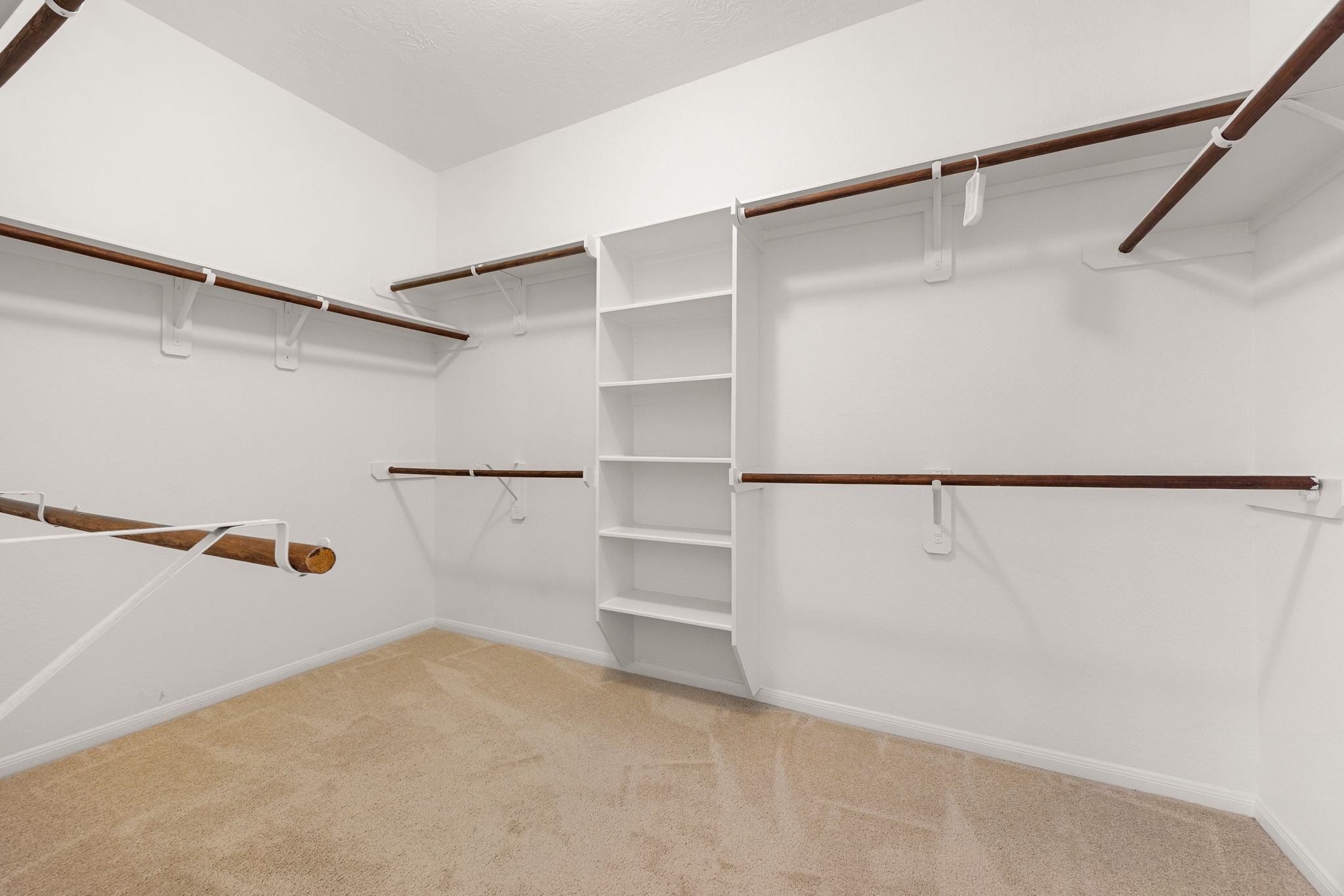 The generous walk-in closet keeps everything organized with a built-in shelving tower and double hanging rods along multiple walls.
