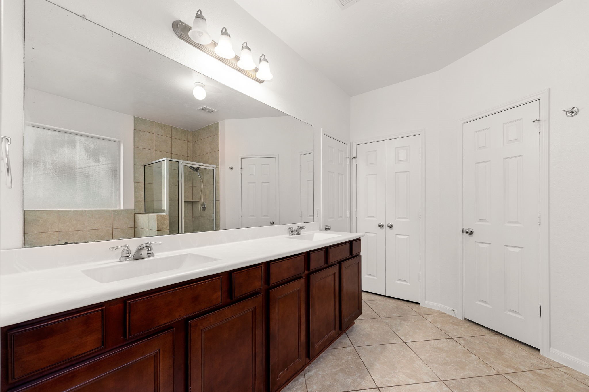 The ensuite bath pairs rich cherry-tone cabinetry with dual sinks and an expansive vanity mirror, plus a linen closet for extra storage.
