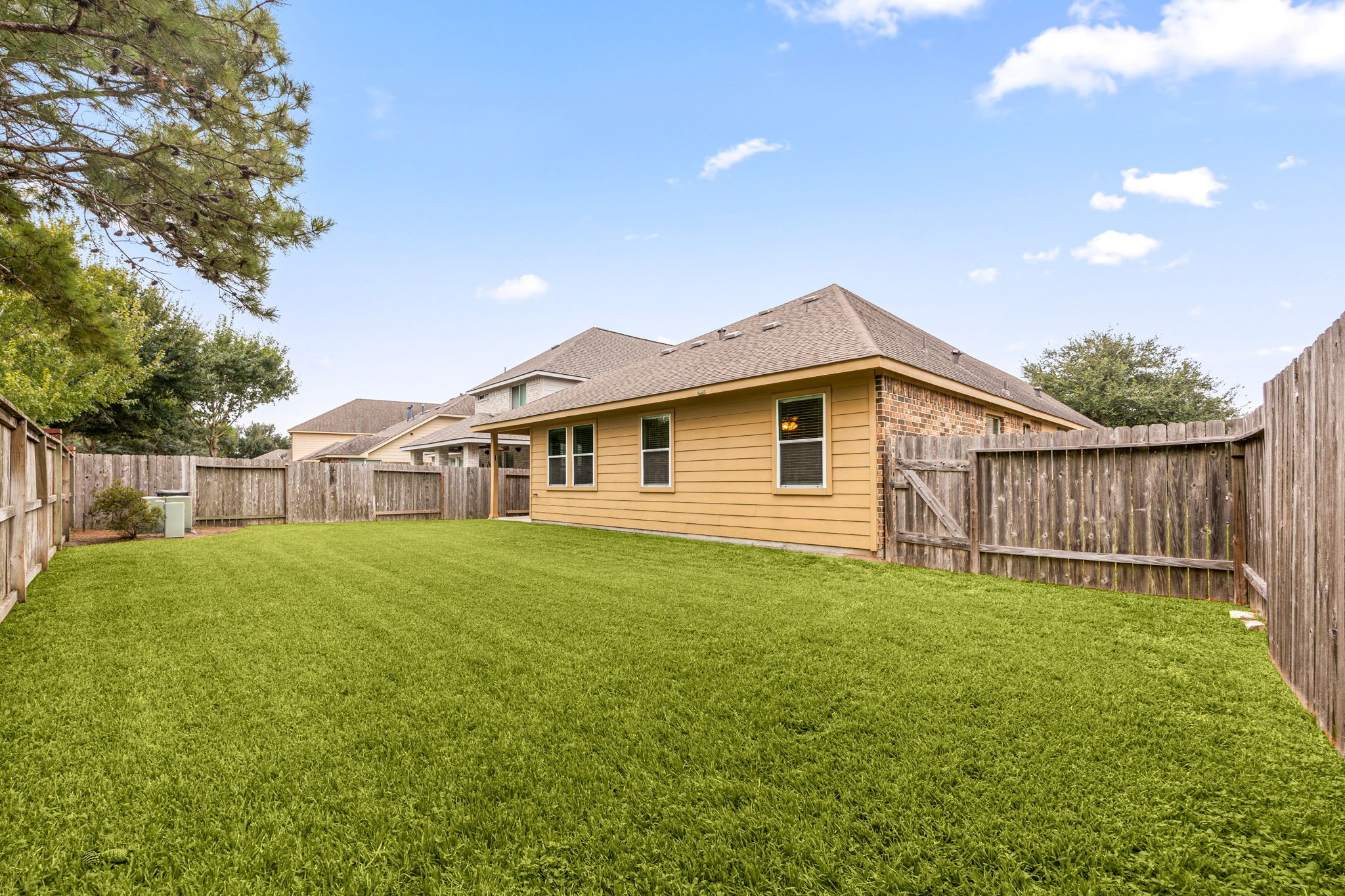 The spacious backyard wraps alongside the home, with privacy fencing, a side gate, and mature trees framing the view.