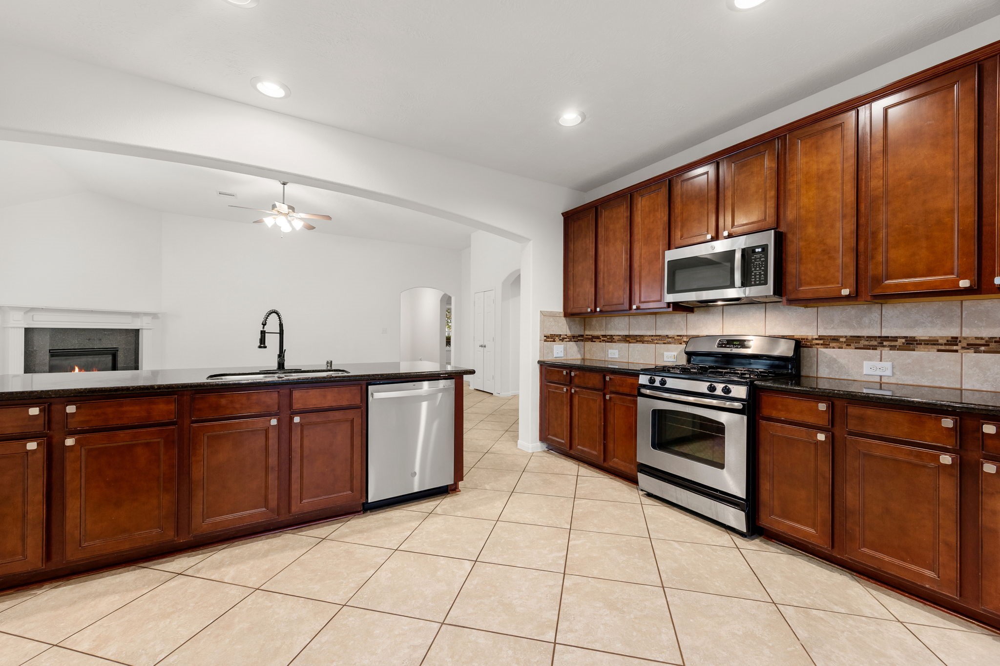 A gas range and built-in microwave are surrounded by gleaming granite countertops, abundant cabinetry, and a tile backsplash accented with a mosaic band. A gas range and built-in microwave are surrounded by gleaming granite countertops, abundant cabinetry, and a tile backsplash accented with a mosaic band.