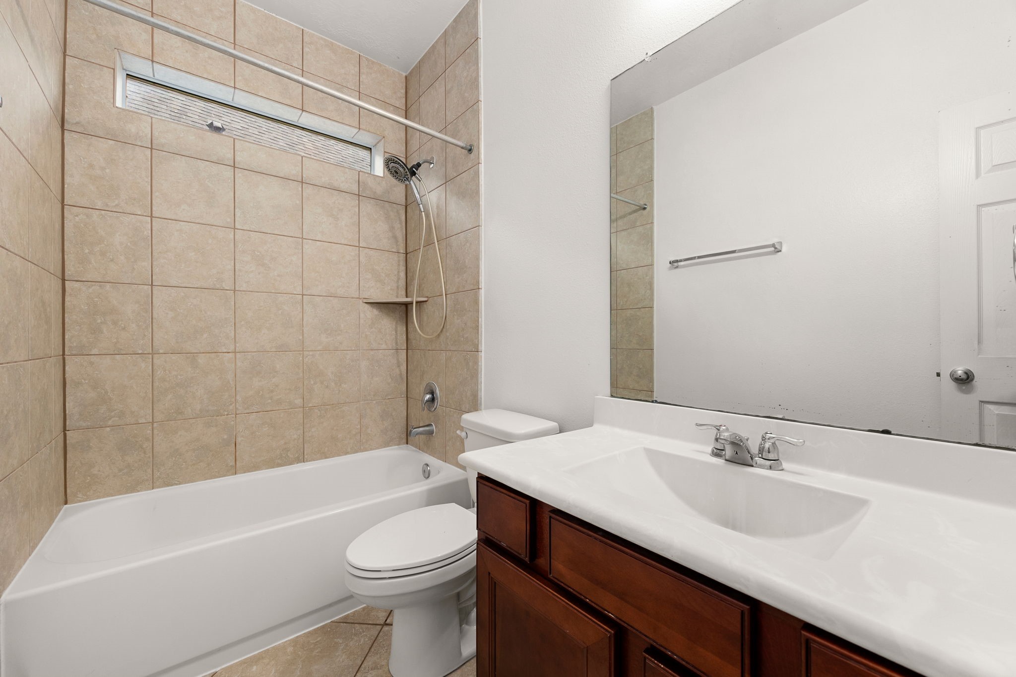 The secondary bathroom features cherry-tone cabinetry, a wide vanity mirror, and a tub/shower combination with a tile surround, a handheld showerhead, and a transom window.