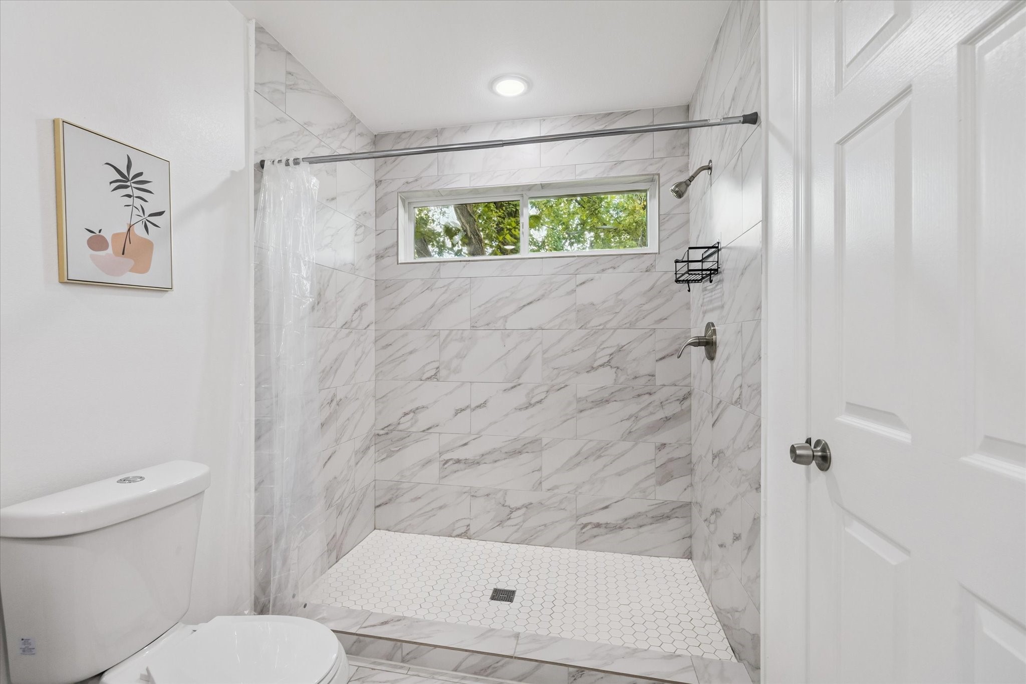The primary bathroom features a spacious walk-in shower with floor-to-ceiling marble-look tile and white hexagon tile flooringelevating both style and function.