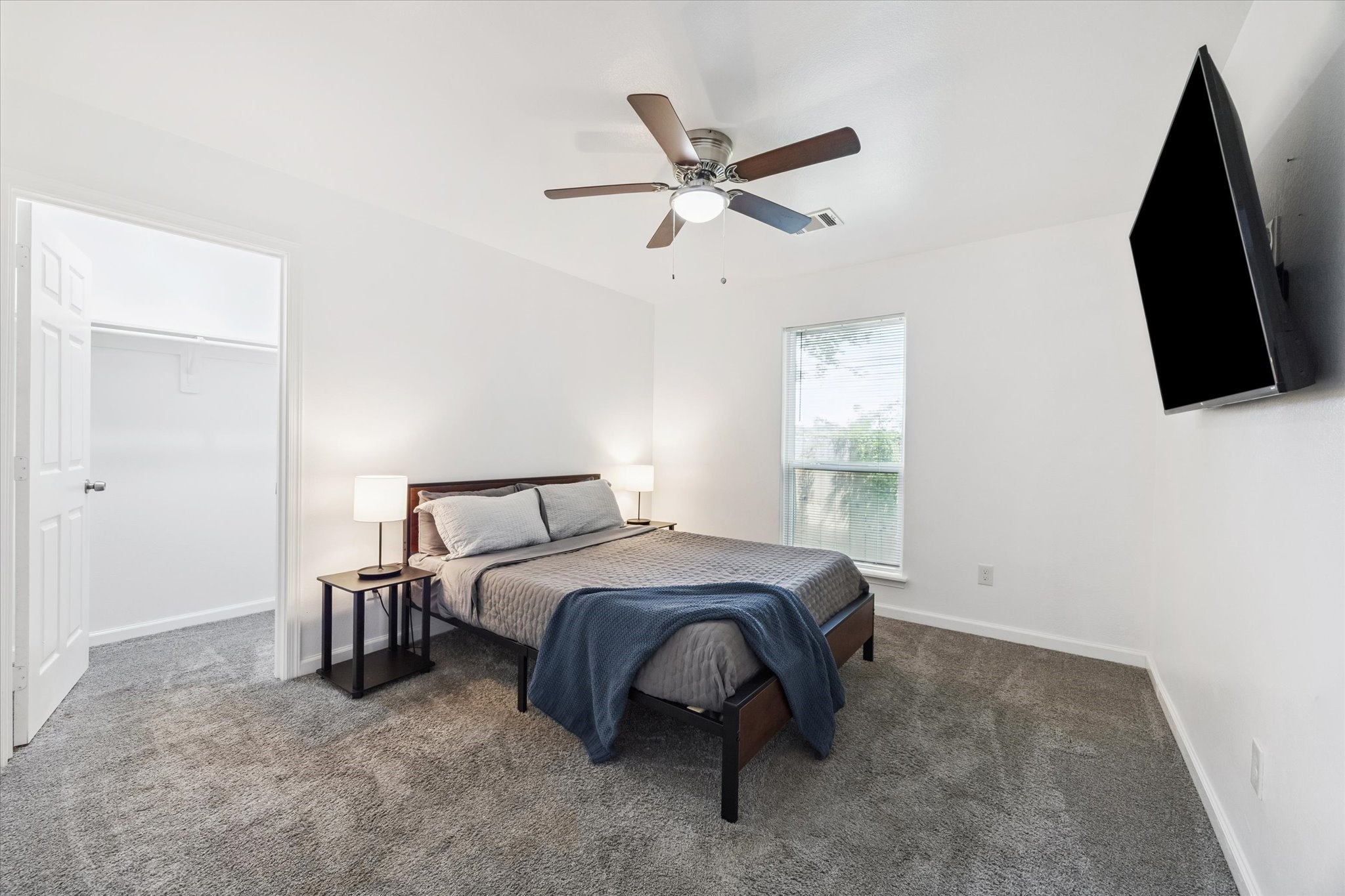 This secondary bedroom features a spacious walk-in closet, a large window that brings in natural light, and a ceiling fan with a light kit for added comfort. Plush carpeting and neutral finishes make it move-in ready.