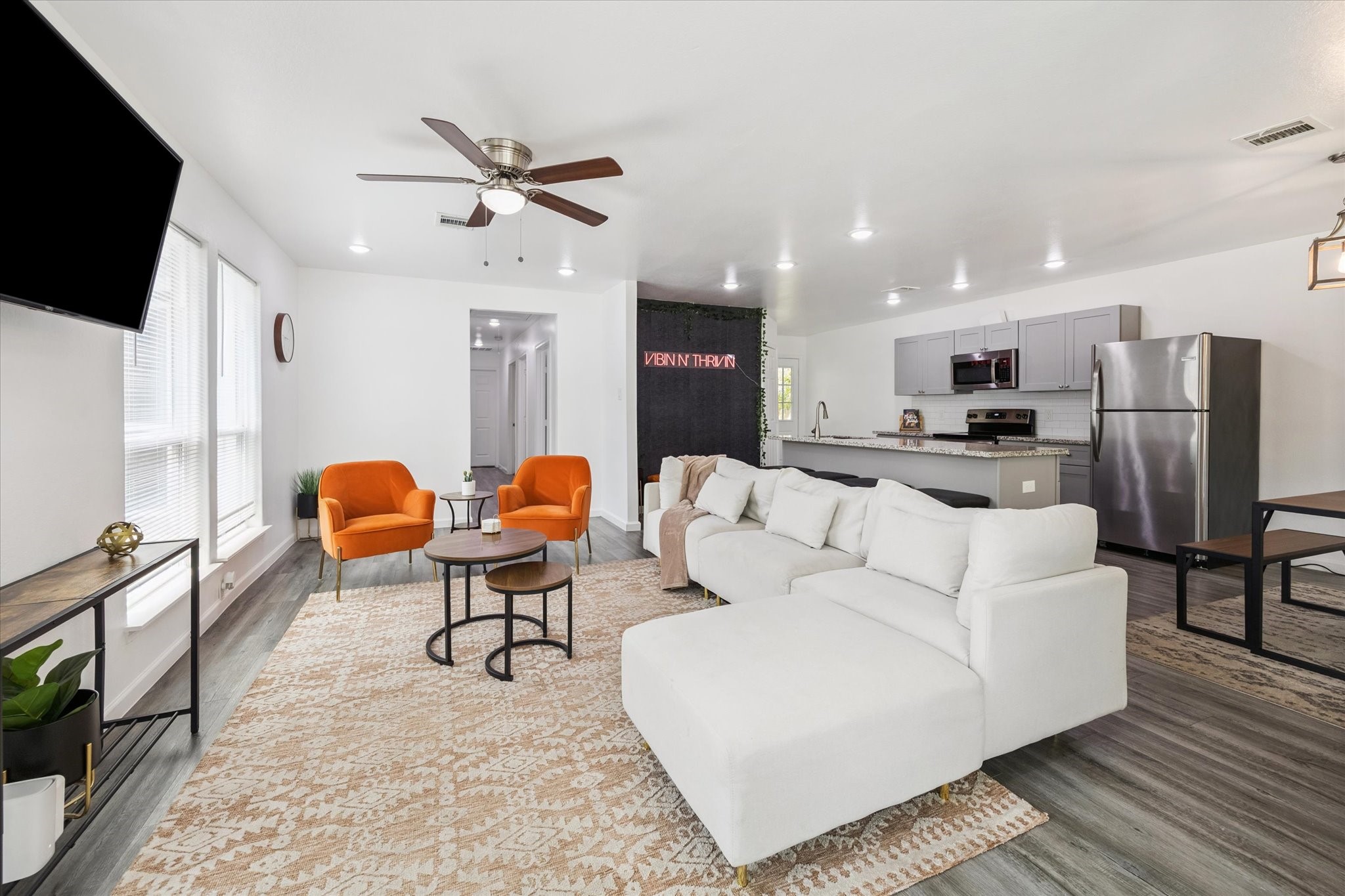 This light-filled living space features durable wood-look flooring, a ceiling fan with integrated light kit, and a hallway that connects seamlessly to all bedrooms and the rest of the home. Large windows line the wall, keeping the space bright while still offering privacy.