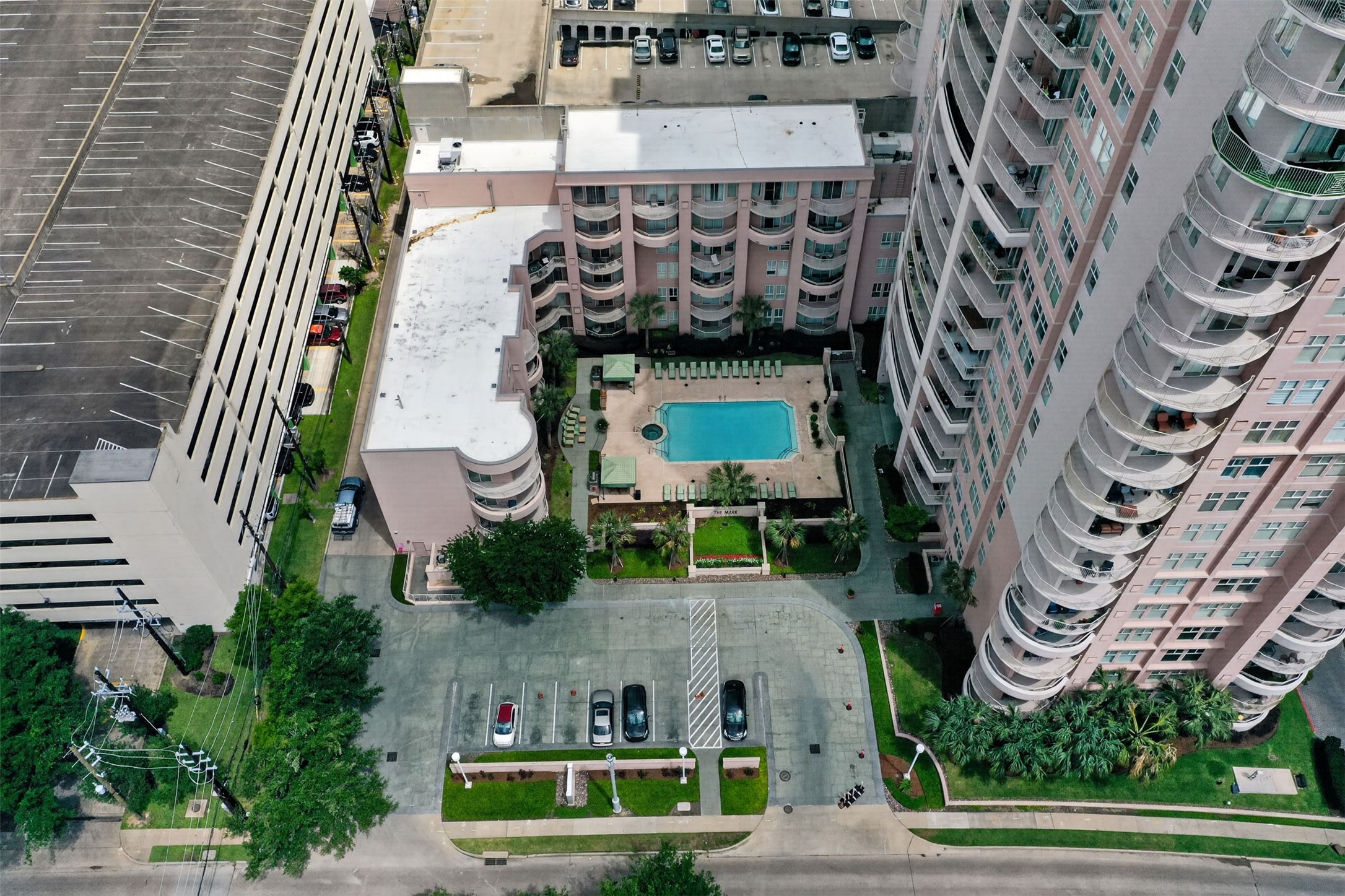 High-rise urban living with a central courtyard featuring a sparkling pool, surrounded by lush greenery and ample parking.