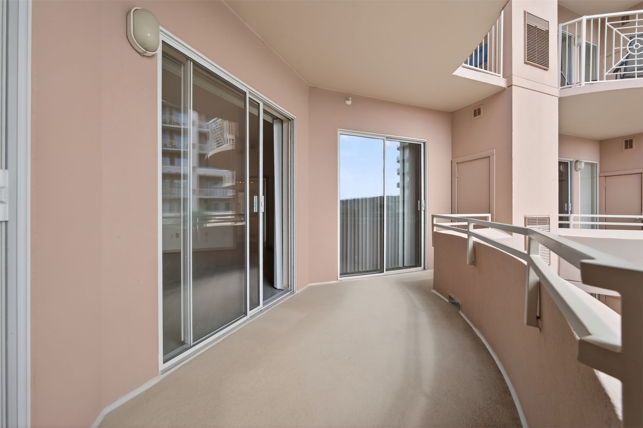 Spacious curved balcony with sliding glass doors and a modern railing, perfect for enjoying outdoor relaxation. The balcony also features two additional storage closets.