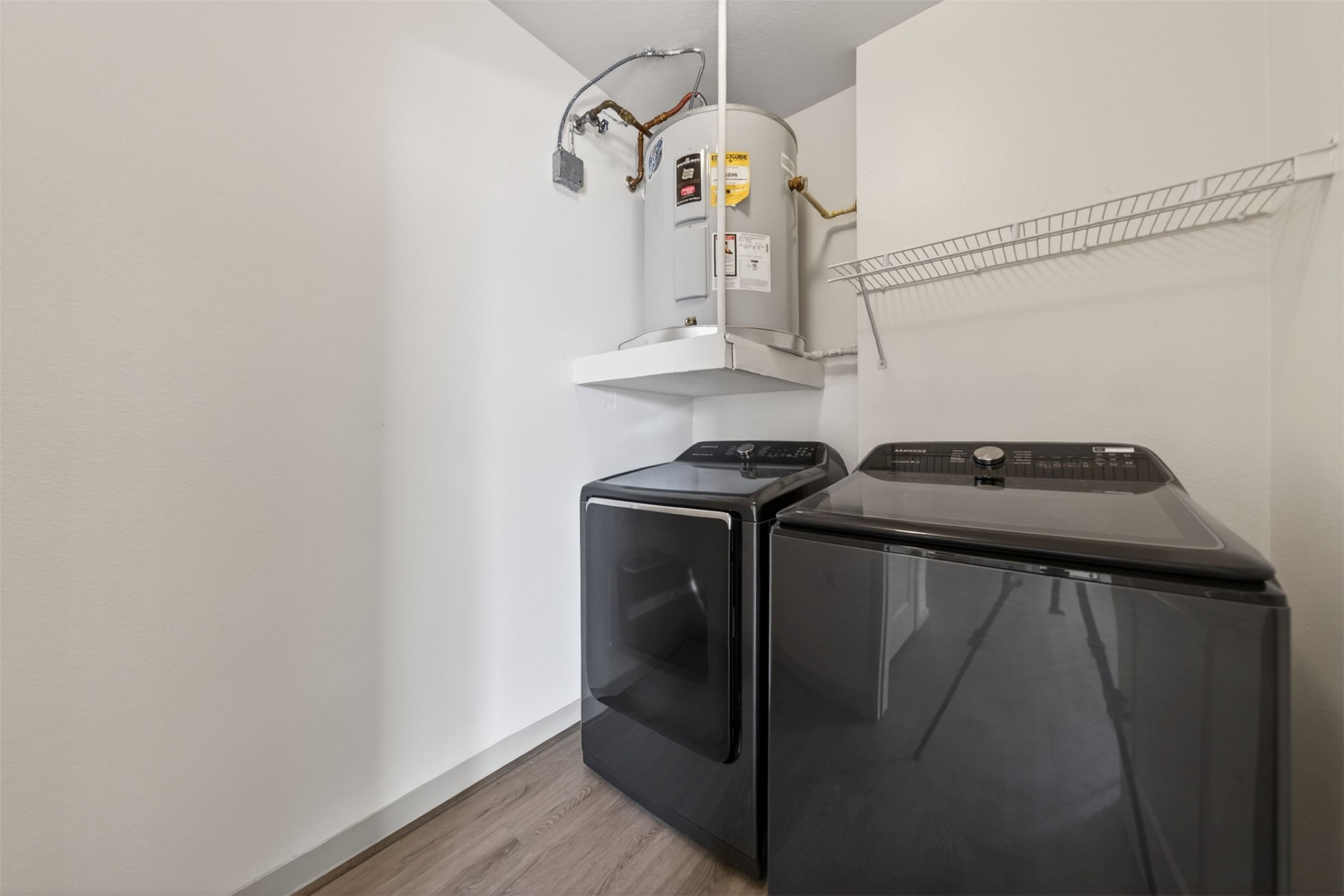 Modern laundry room with sleek appliances that are included, a water heater, and a convenient wire shelf for storage.