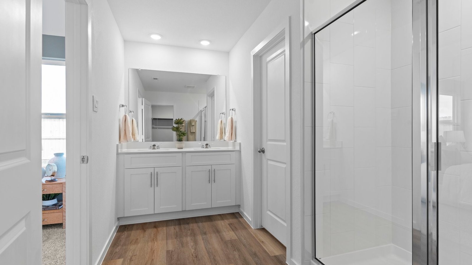 Modern primary bathroom with double vanities, quartz countertops, and a glass-enclosed shower with a walk-in closet.