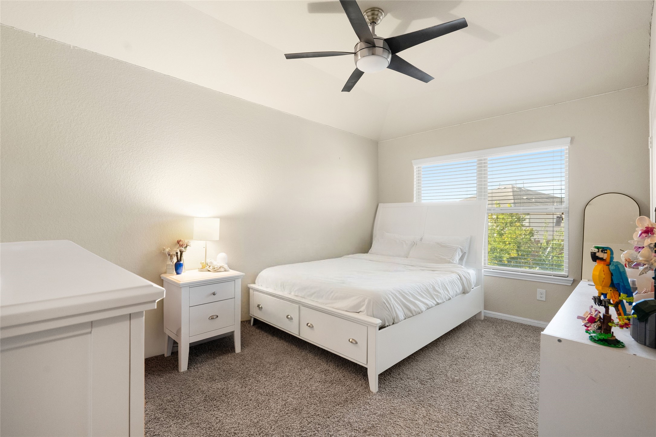 Bright and inviting bedroom with a vaulted ceiling, modern ceiling fan, and large window offering plenty of natural light.
