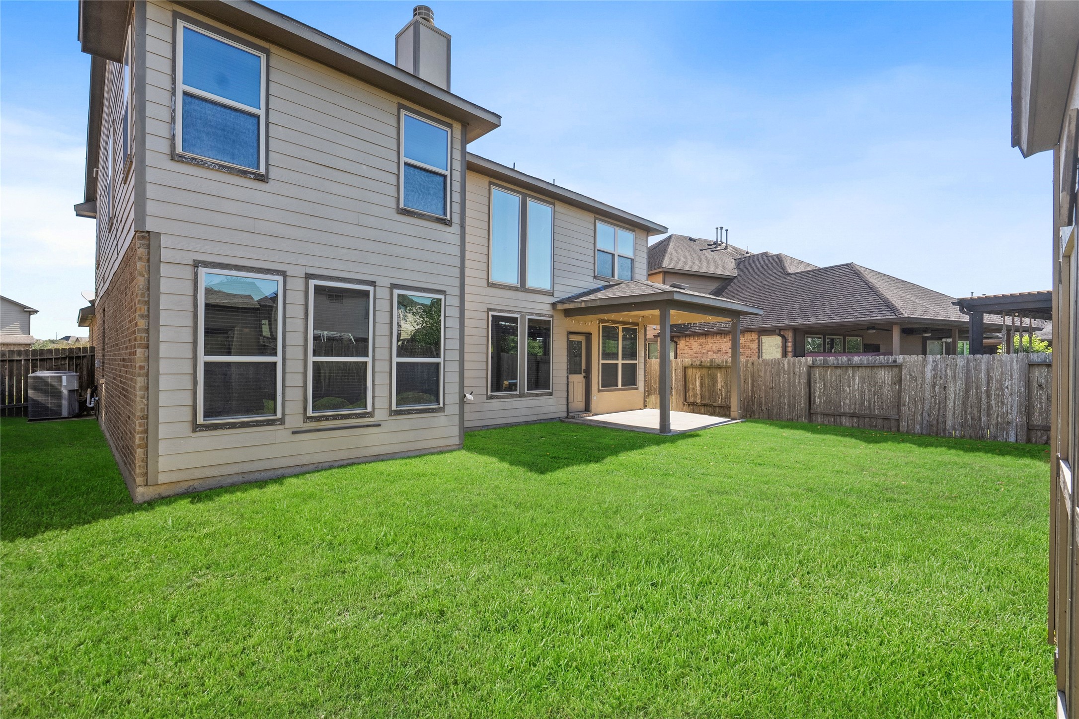 Spacious backyard with a well-maintained lawn, featuring a two-story home with large windows and a covered patio, perfect for outdoor relaxation and entertaining.