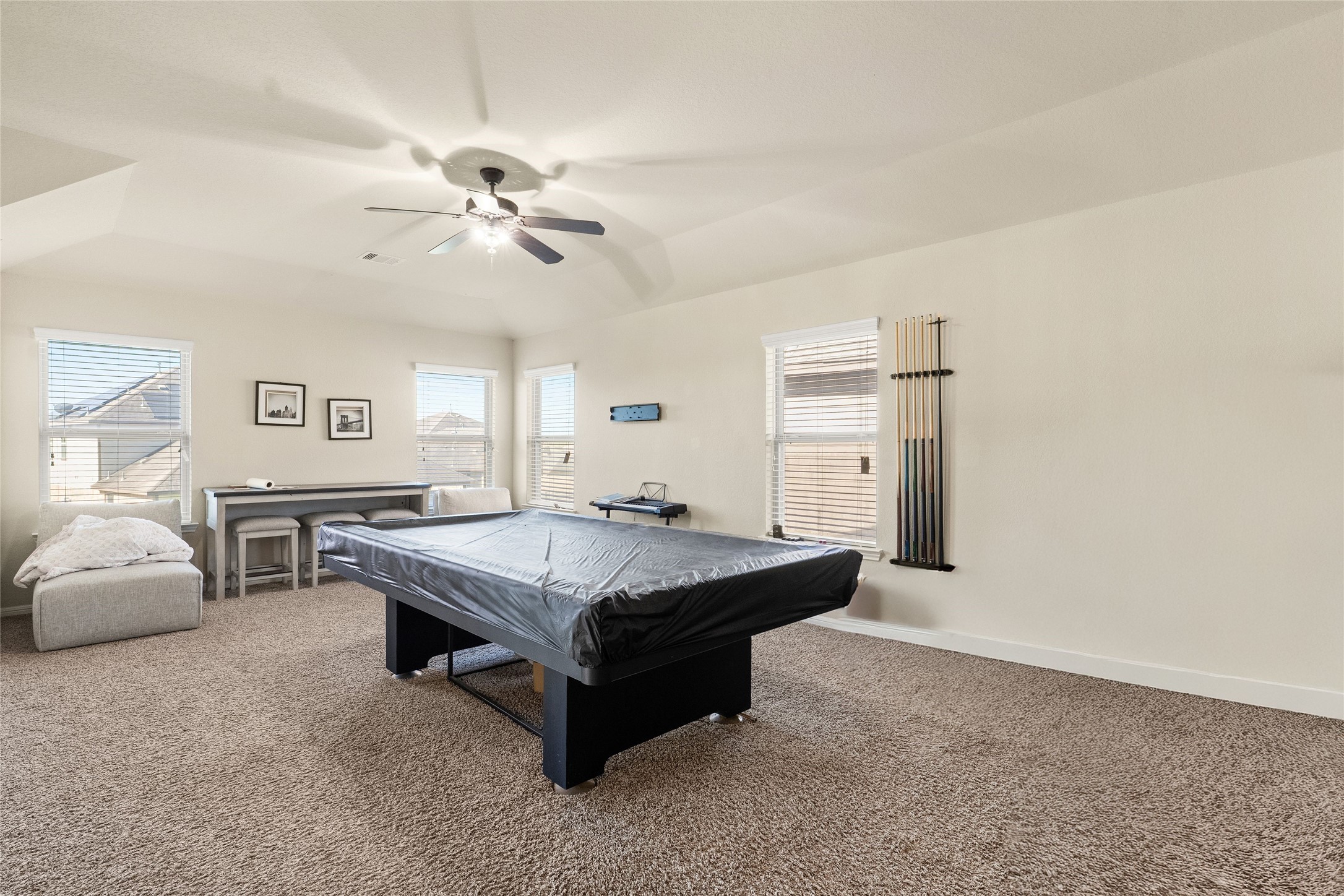 Spacious game room featuring a central pool table, plush carpeting, and ample natural light from multiple windows, ideal for entertainment and relaxation.