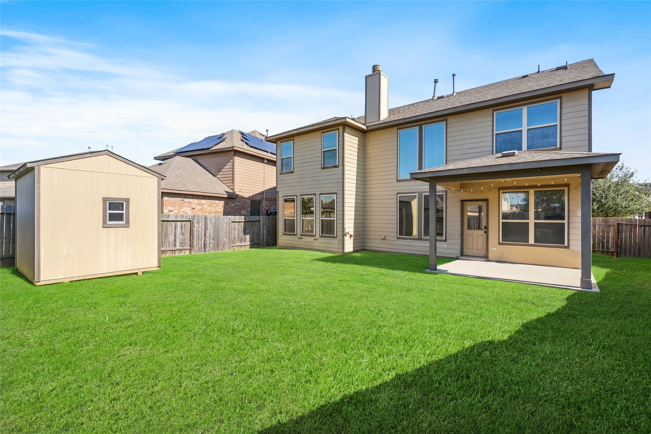 Spacious backyard featuring a well-maintained lawn, a convenient storage shed, and a covered patio perfect for outdoor gatherings.