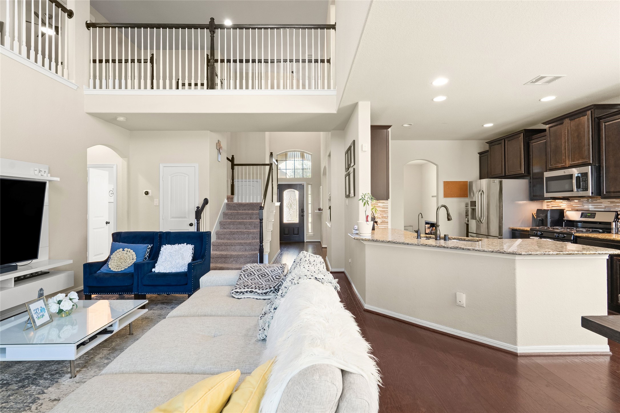 Spacious open-concept living area with high ceilings, a cozy loft, and a modern kitchen featuring granite countertops and stainless steel appliances.
