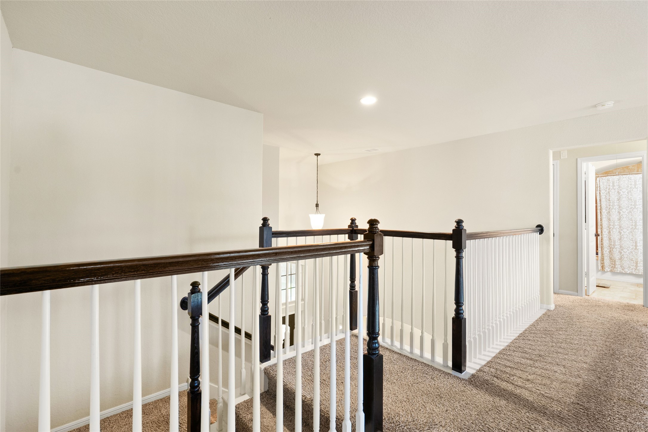 Bright and airy upstairs landing featuring elegant dark wood railing and plush carpeting, leading to a cozy bedroom and bathroom.