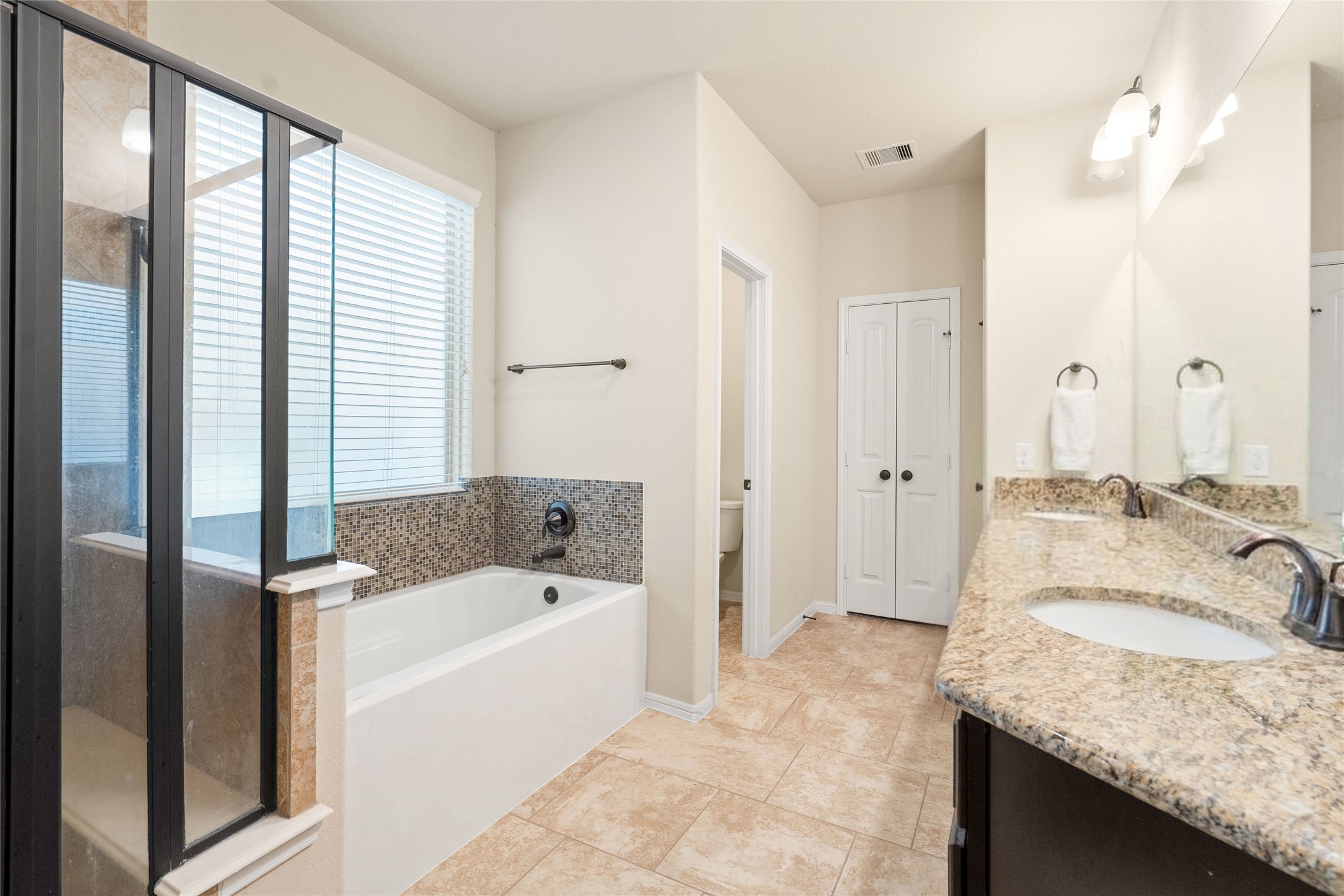 Spacious bathroom with elegant granite countertops, dual sinks, a luxurious soaking tub, and a separate glass-enclosed shower.