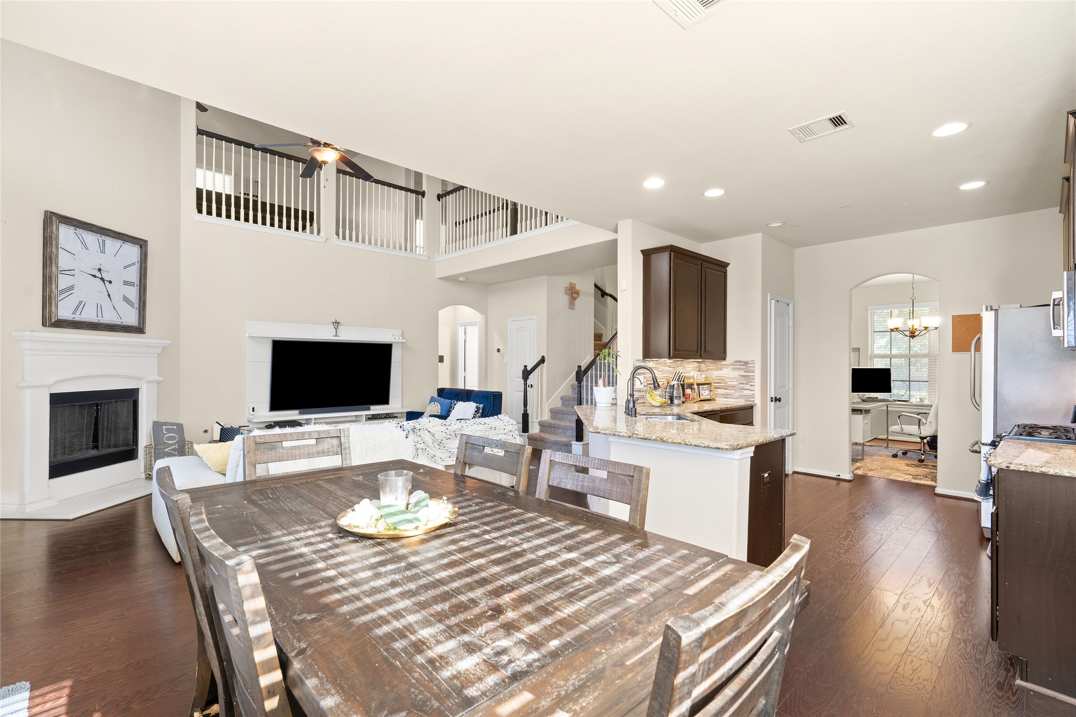 Spacious open-concept living area with high ceilings, featuring a cozy fireplace, modern kitchen with granite countertops, and ample natural light.
