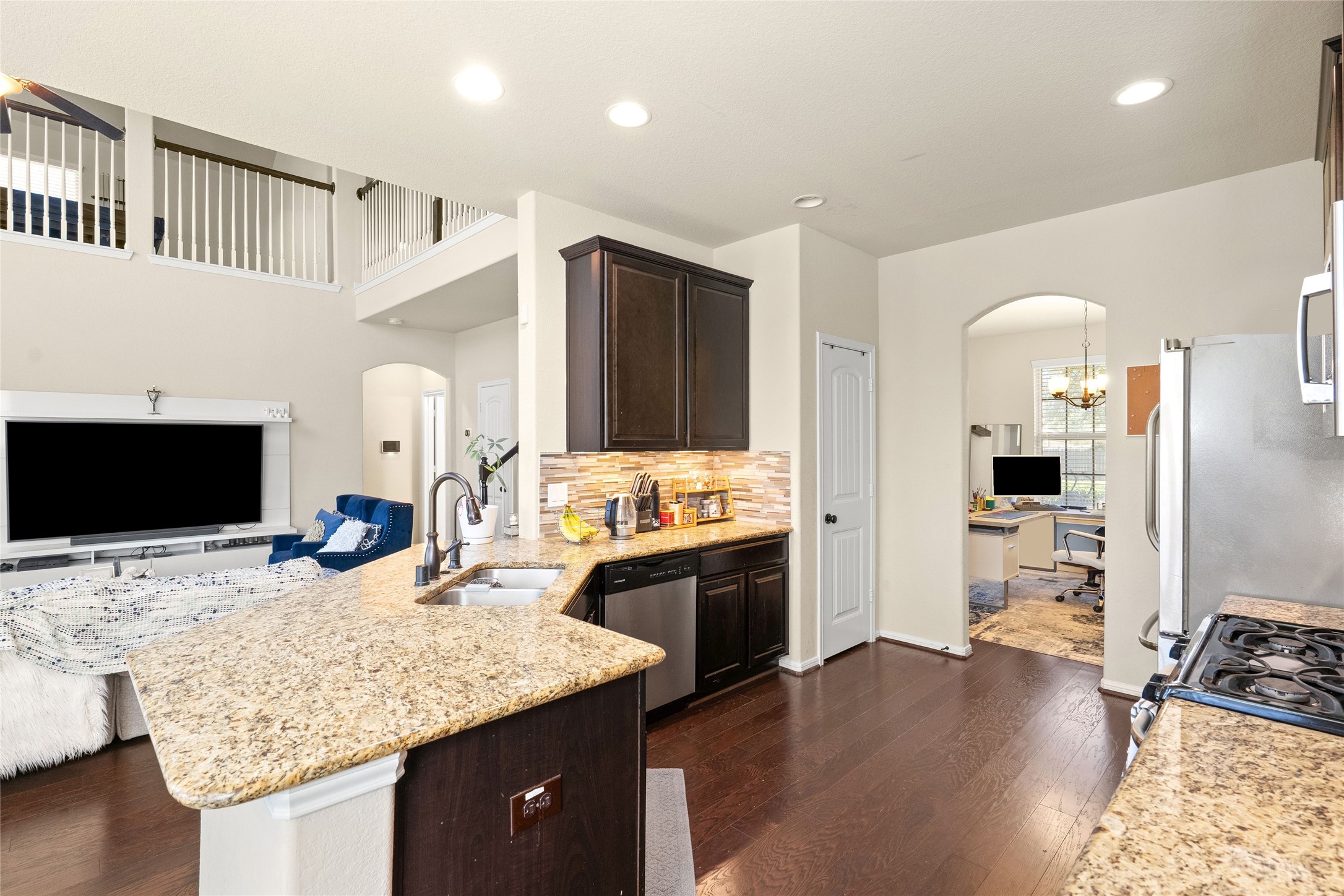 Spacious kitchen with elegant granite countertops, dark cabinetry, and stainless steel appliances, seamlessly flowing into a cozy living area with an adjacent home office space.