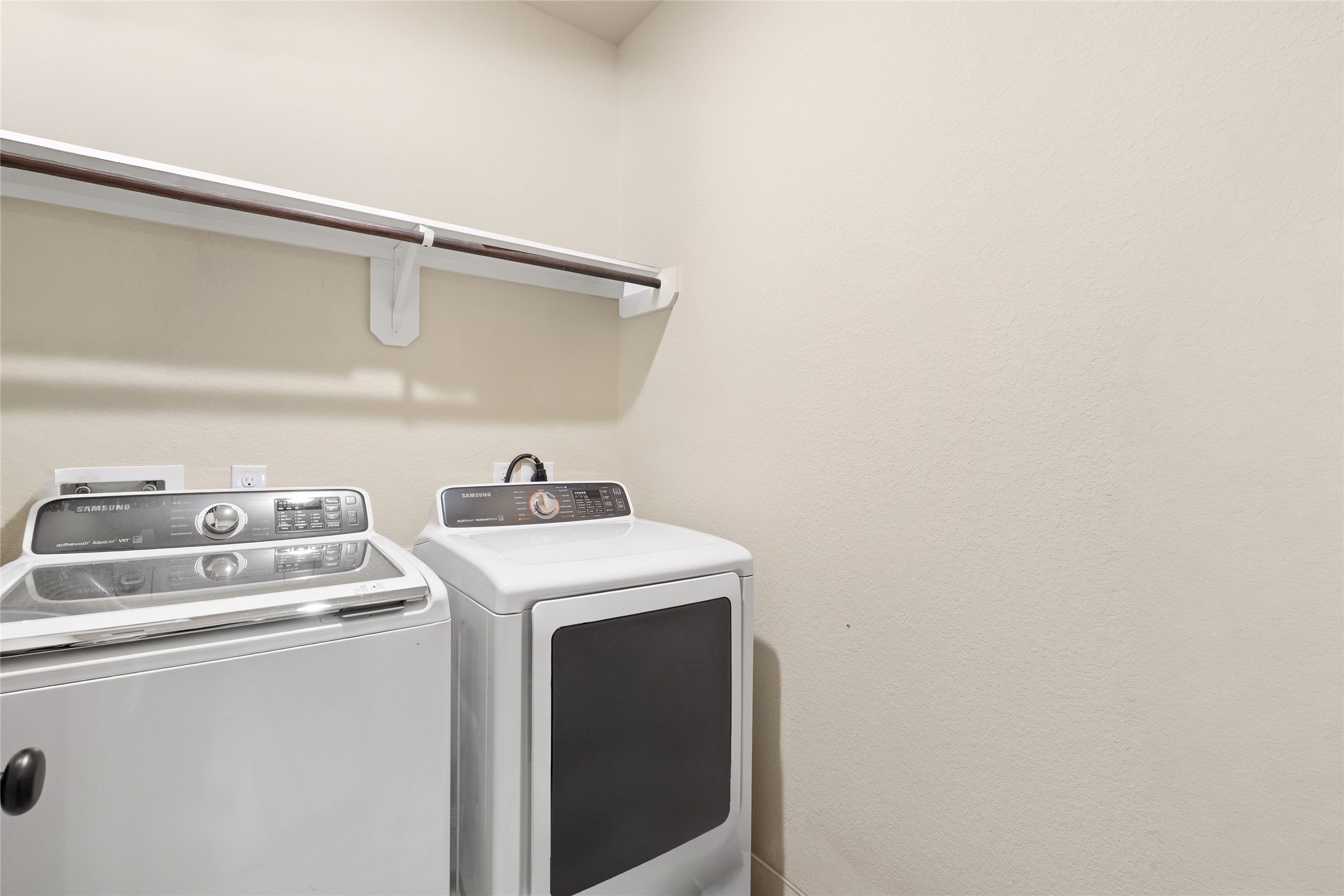 Spacious laundry room equipped with modern washer and dryer, complemented by a convenient overhead shelf for storage.