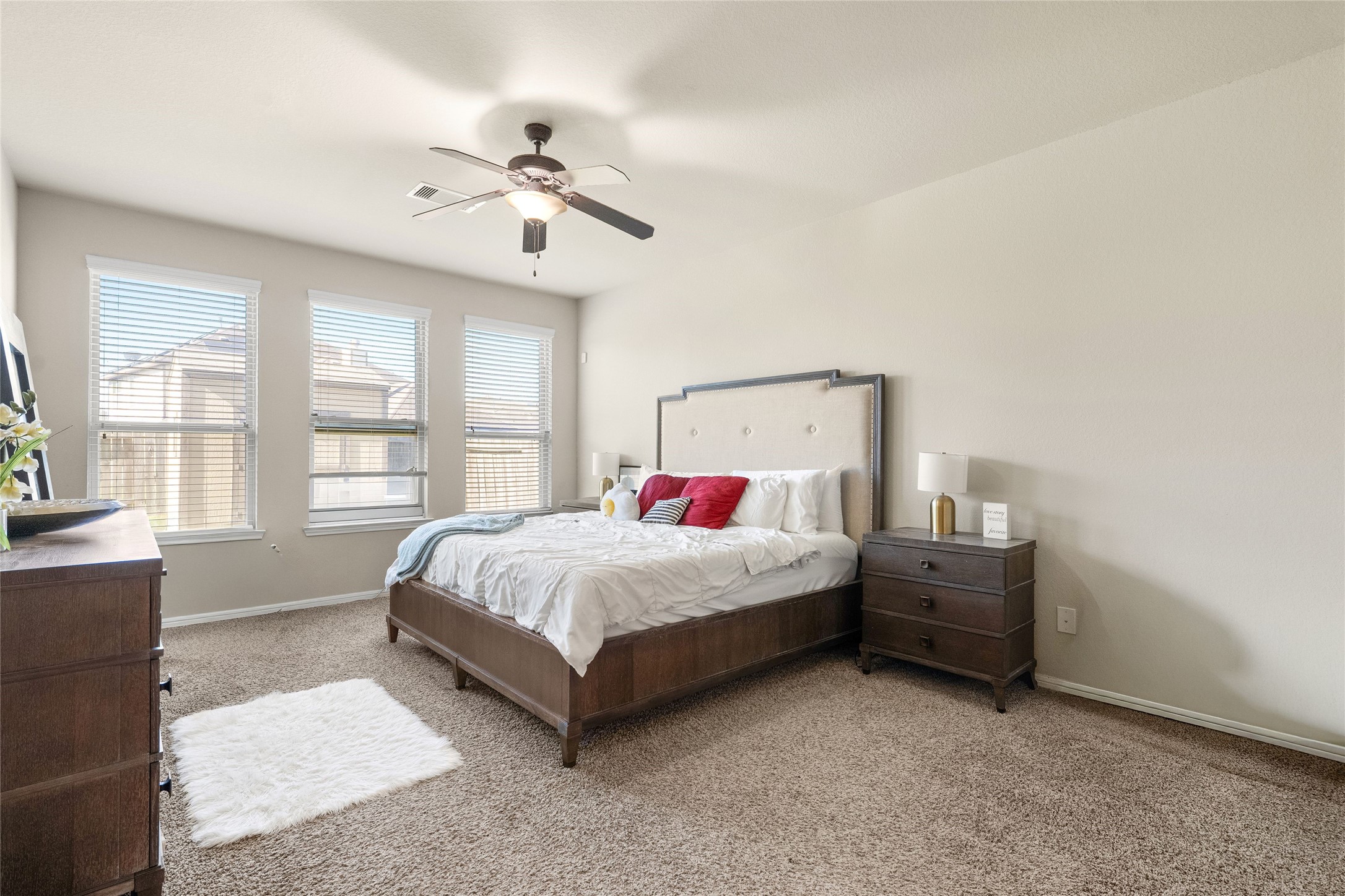 Spacious bedroom with plush carpeting, abundant natural light from three large windows, and a stylish ceiling fan.