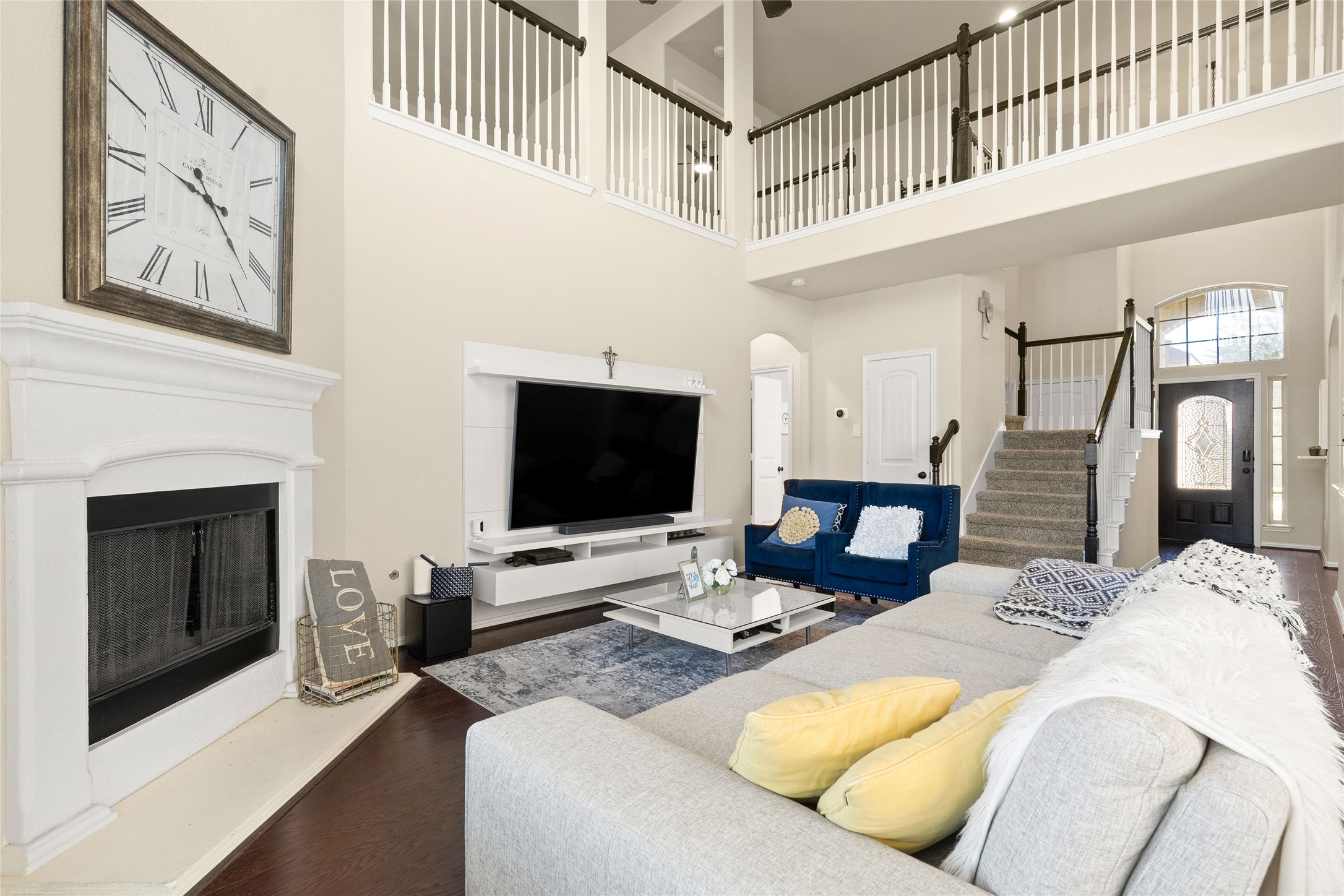 Elegant living room with high ceilings, featuring a cozy fireplace, modern entertainment center, and stylish seating. A grand staircase leads to the upper level, enhancing the open-concept design.