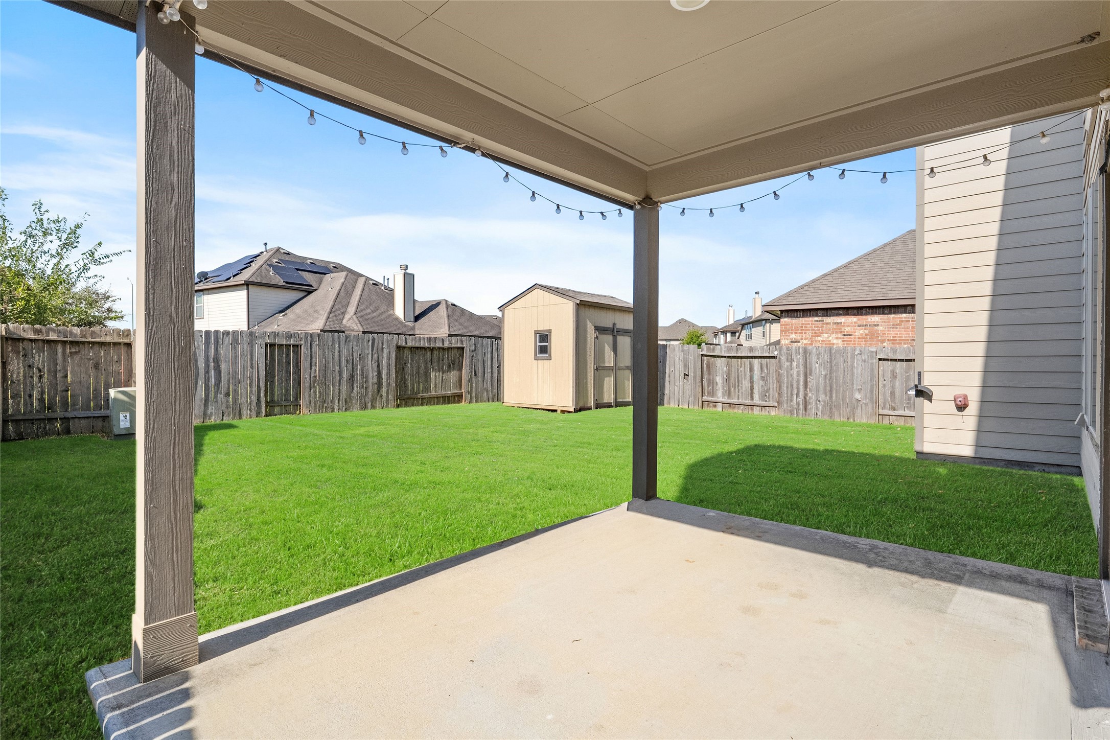 Spacious backyard featuring a covered patio with string lights, perfect for outdoor gatherings, and a large storage shed for added convenience.