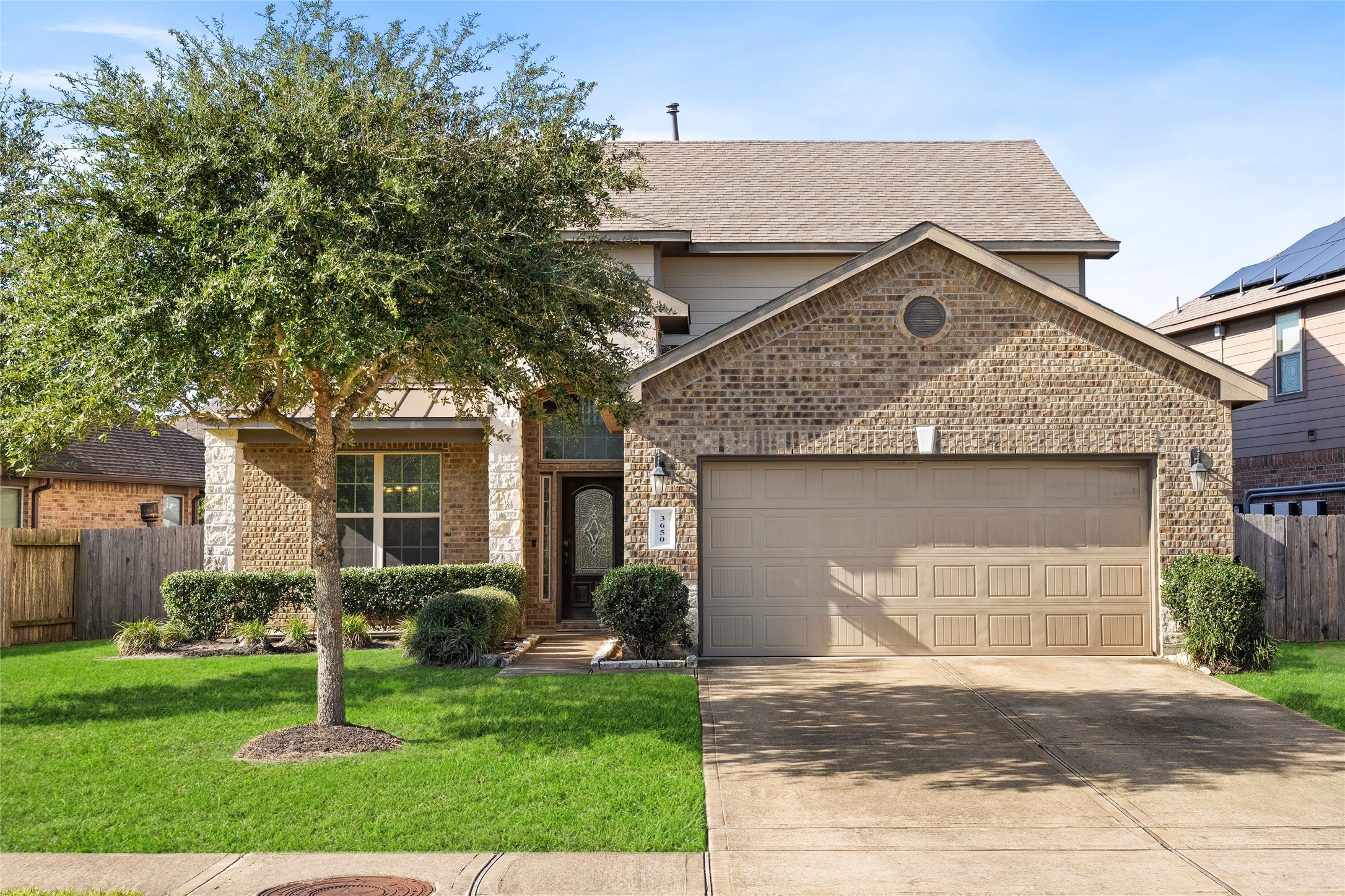Charming two-story home with a warm brick faade, inviting entryway, and well-maintained landscaping, featuring a spacious two-car garage and a mature tree providing shade.