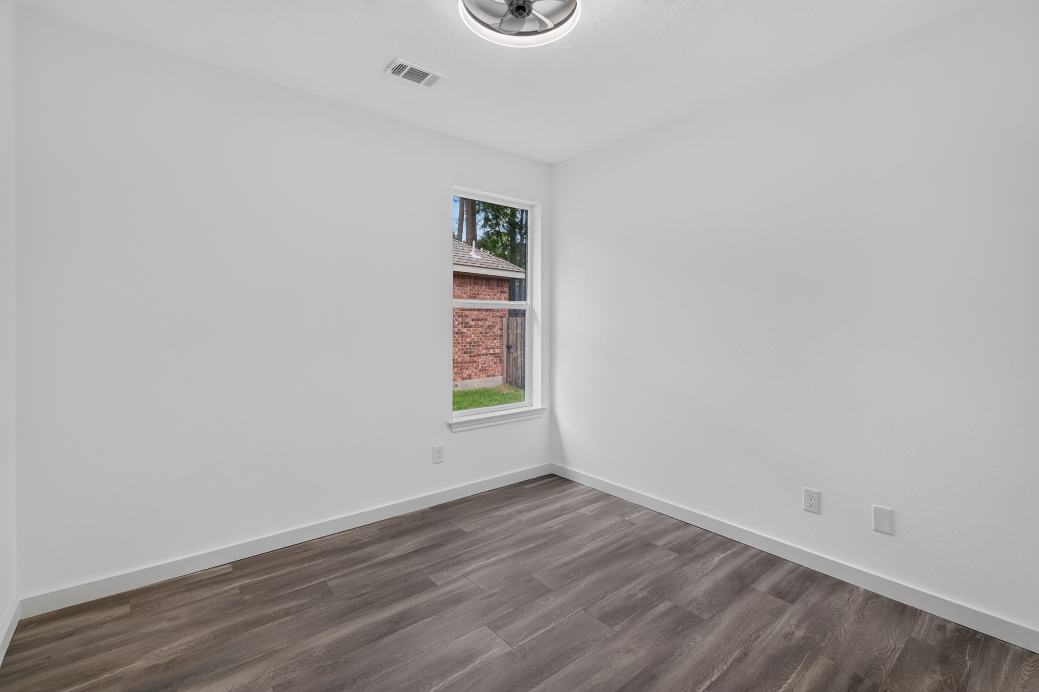A well-sized secondary bedroom at 18 Griffin Hill Court offers a clean canvas for personalization, featuring white walls, a ceiling fan for comfort, and beautiful dark hardwood-style floors throughout. With easy access to the hallway and nearby bathrooms, this room is ideally positioned within the home's private and well-designed bedroom wing.
