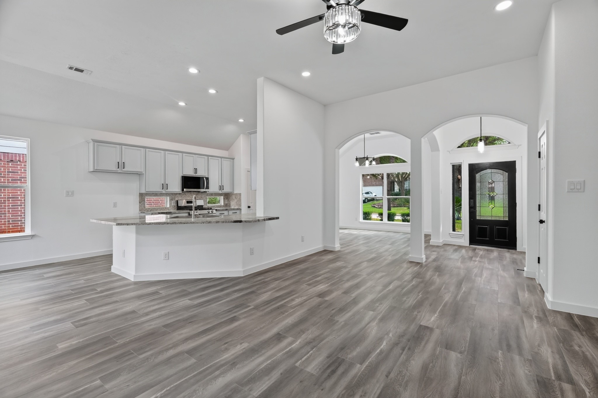 A seamless open-concept design connects the gourmet kitchen to the main living areas at 18 Griffin Hill Court. This perspective from the kitchen shows the expansive living space beyond, demonstrating how this home's layout perfectly supports an active family lifestyle while keeping the chef connected to the action. Dark hardwood-style floors tie everything together.