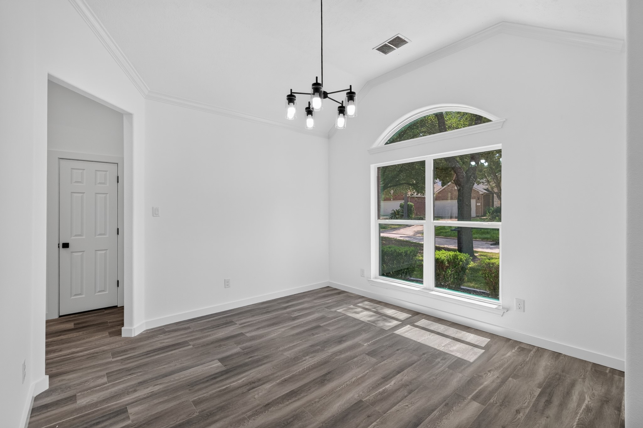 This elegant dining area features an arched window that floods the space with beautiful natural light, rich dark hardwood-style flooring, and a stunning designer chandelier overhead. With generous proportions, this dining space at 18 Griffin Hill Court is ideal for hosting family dinners and entertaining guests in style and comfort.