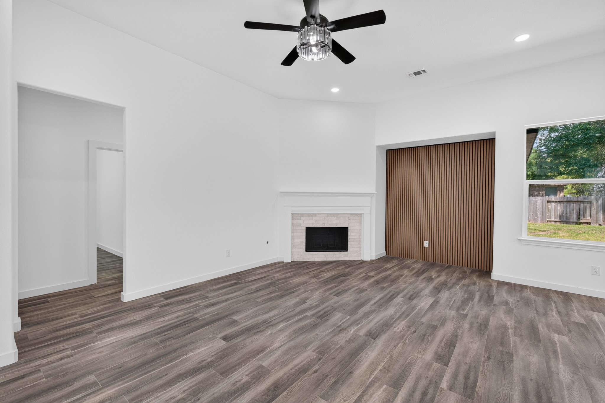 Another perspective of the open-concept family room at 18 Griffin Hill Court showcases the ceiling fan, dramatic fireplace focal point, and expansive dark hardwood-style floors. The generous square footage of this living area provides ample room for comfortable furniture arrangements and reflects the home's thoughtful, livable open floor plan.