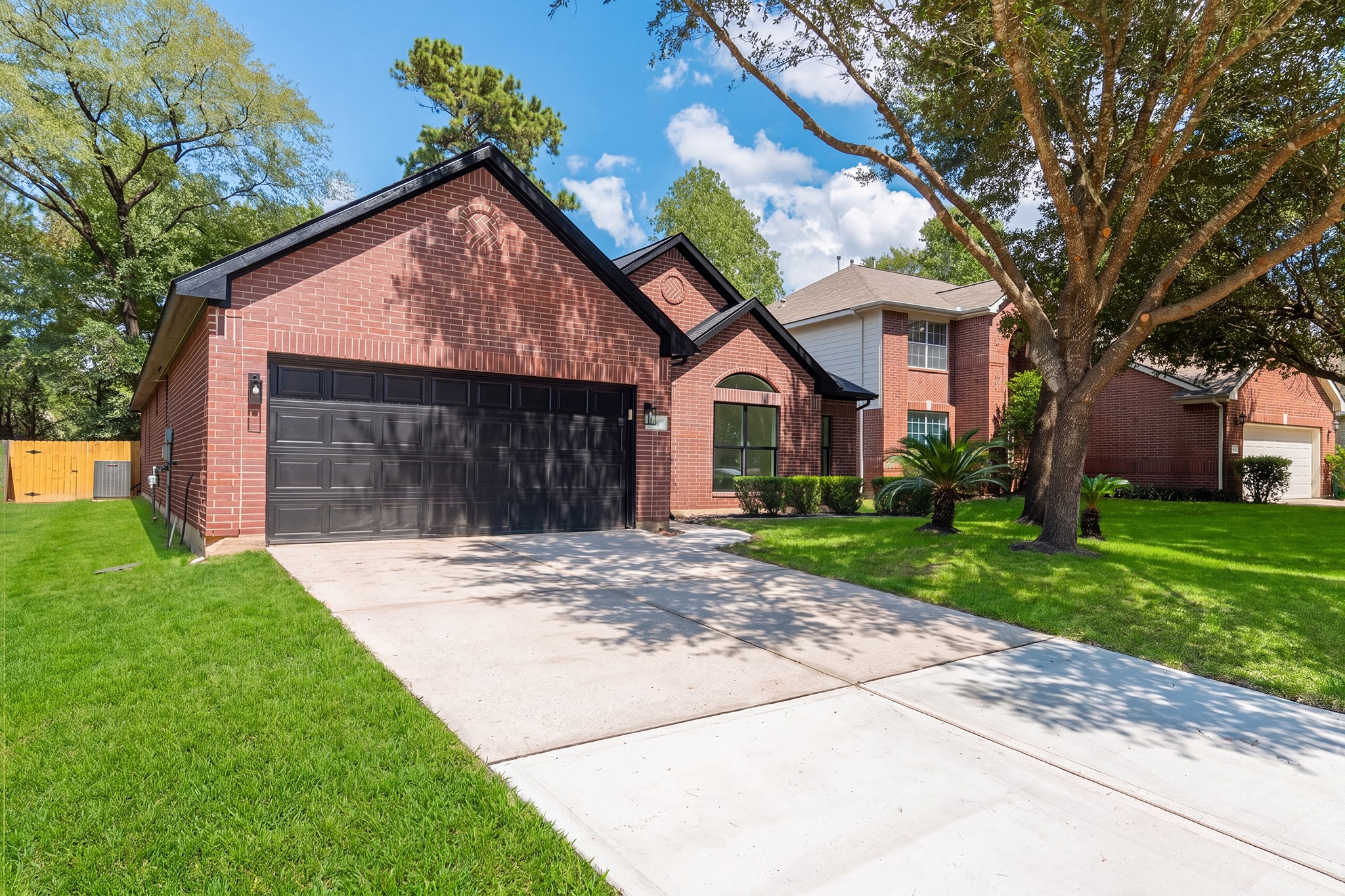 Daytime curb appeal at its finest  18 Griffin Hill Court shines under a bright blue Texas sky. This beautifully maintained single-story brick home features lush green landscaping, a magnificent mature oak tree in the front yard, and a spacious two-car garage, creating outstanding first impressions in this desirable Spring neighborhood.