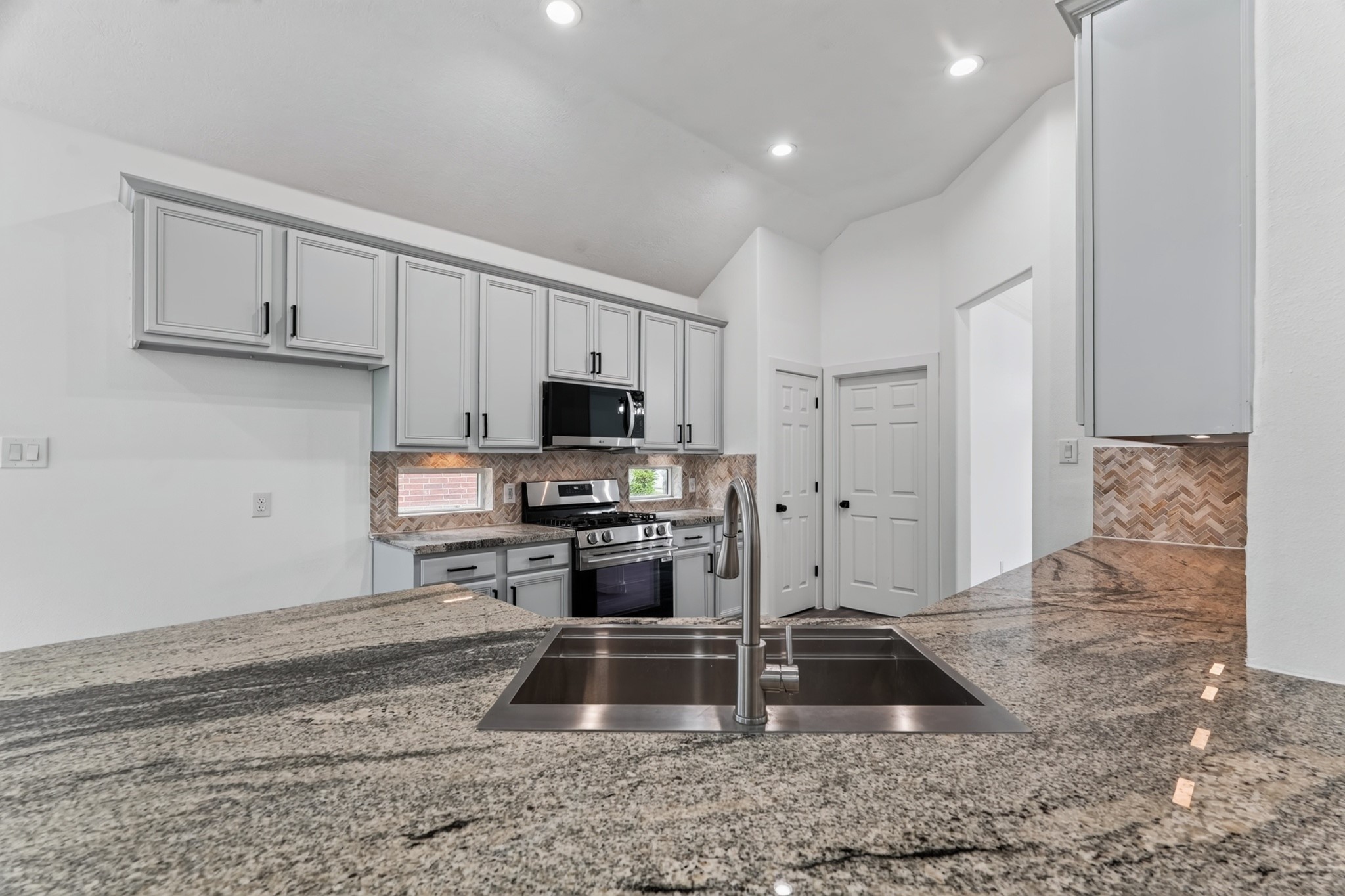The beautifully appointed kitchen at 18 Griffin Hill Court features grey shaker cabinetry, light stone countertops, and high-end stainless steel appliances. Gold-tone hardware and fixtures add a warm, luxurious finishing touch, while the spacious layout provides everything the home chef needs to cook, entertain, and gather with family and friends.