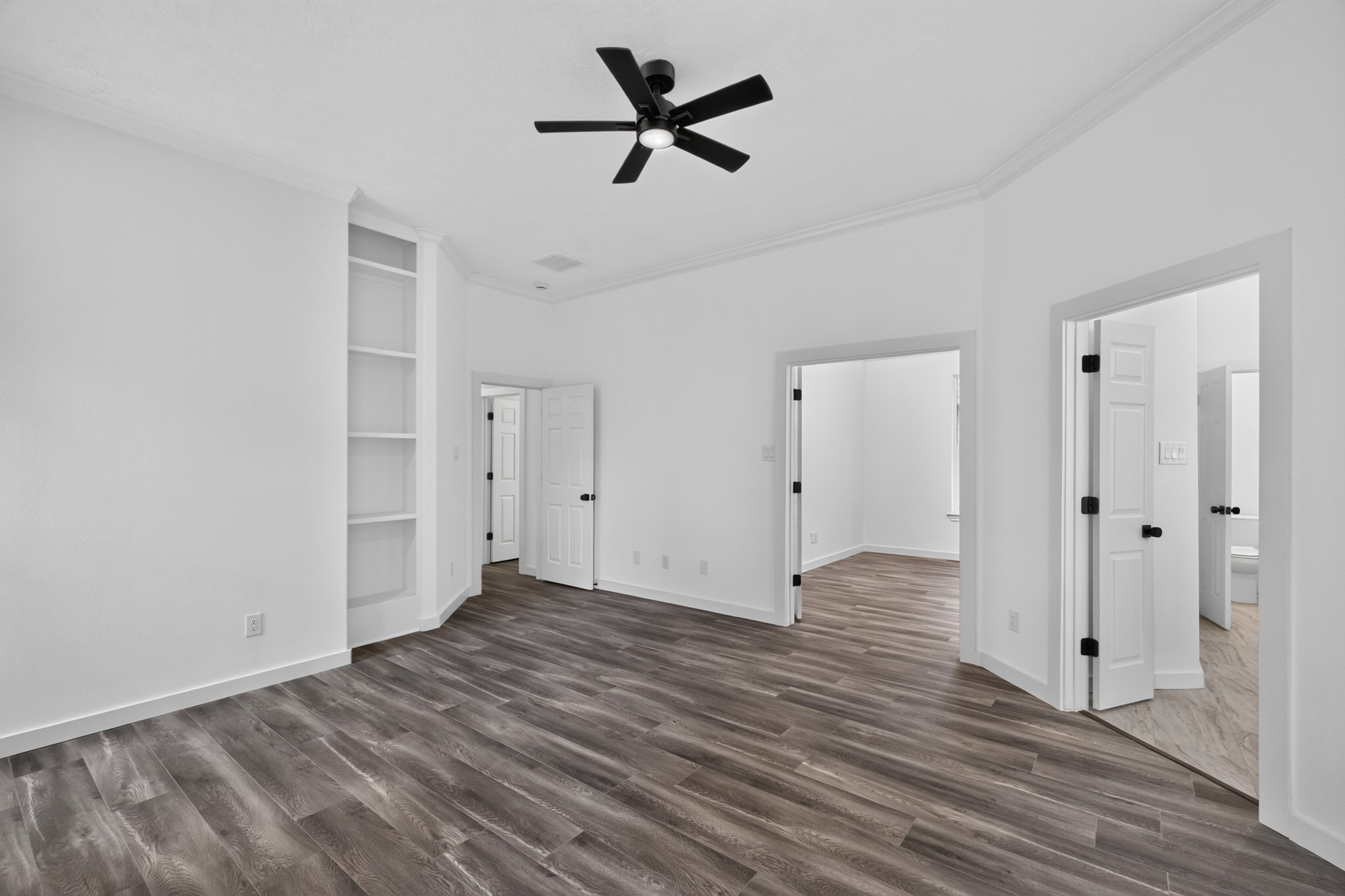 A spacious secondary bedroom at 18 Griffin Hill Court features pristine white walls, a ceiling fan overhead, and gorgeous dark hardwood-style flooring. With ample square footage for a full bedroom suite, this room offers comfort and versatility  ideal for family members, overnight guests, or any lifestyle use you envision for the space.
