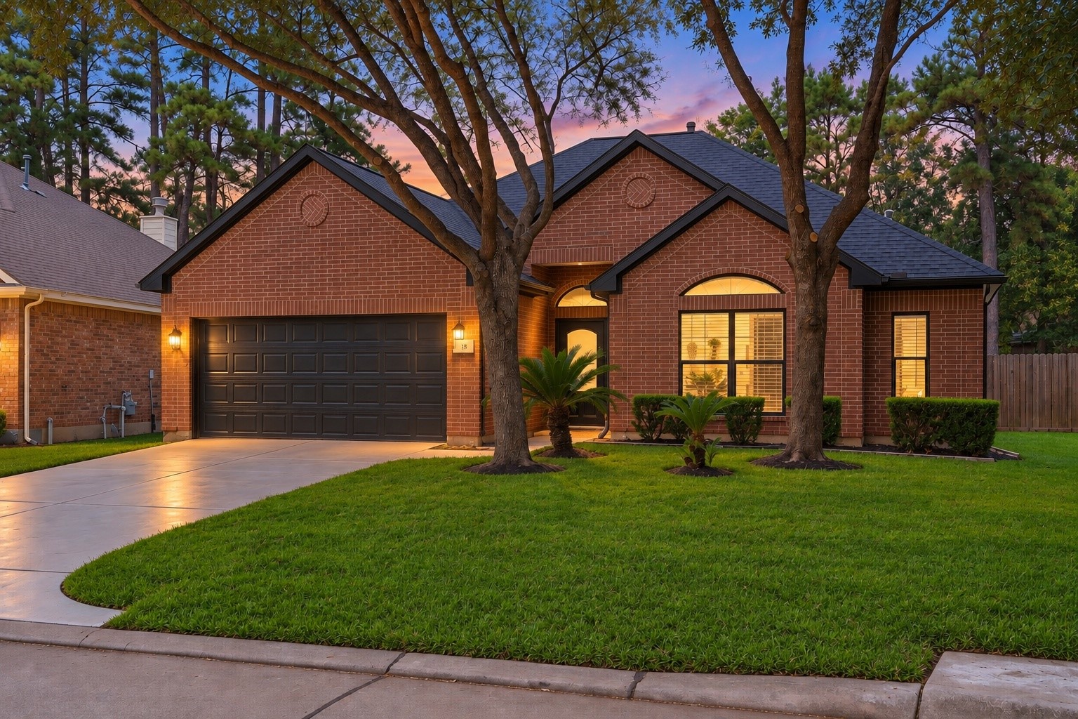 Another breathtaking twilight view of 18 Griffin Hill Court's classic brick facade. The deep purple and pink dusk sky creates a dramatic and romantic backdrop, while warm interior lighting glows invitingly through the windows. Mature trees frame this stunning single-story home in a picturesque evening scene. (PHOTO MAY BE AI ENHANCED.)