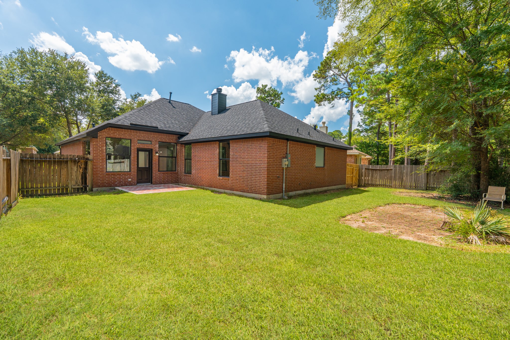 Another angle of the generous backyard at 18 Griffin Hill Court showcases the lush green lawn, mature privacy trees along the perimeter, and the home's solid brick construction. This private outdoor space is the perfect canvas for creating your dream patio, pool area, garden, or outdoor entertainment space in Spring, Texas's warm and sunny climate.