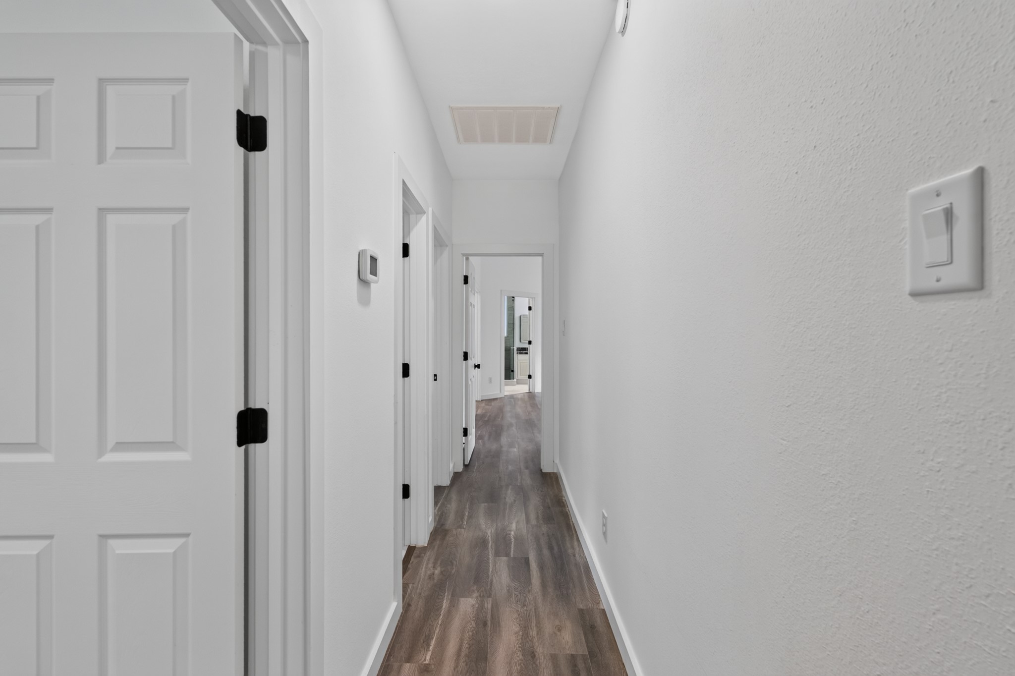 The hallway at 18 Griffin Hill Court connects the home's private bedroom wing with clean architectural lines and easy accessibility. Pristine white walls and dark hardwood-style flooring create a bright, cohesive corridor that flows naturally between rooms  a reflection of the home's thoughtful design and meticulous attention to functional detail.