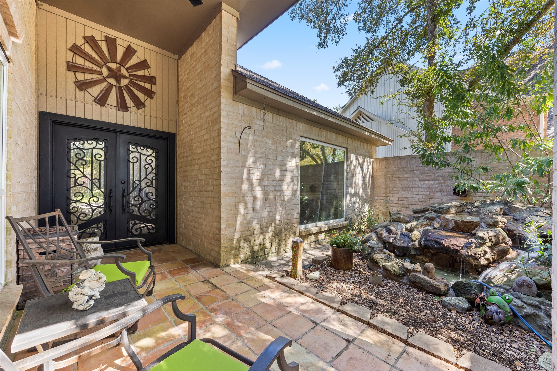 An inviting courtyard features a stone-paved patio, decorative water feature, and striking double entry doors with ornamental ironwork. A charming space to welcome guests or enjoy a quiet moment outdoors.