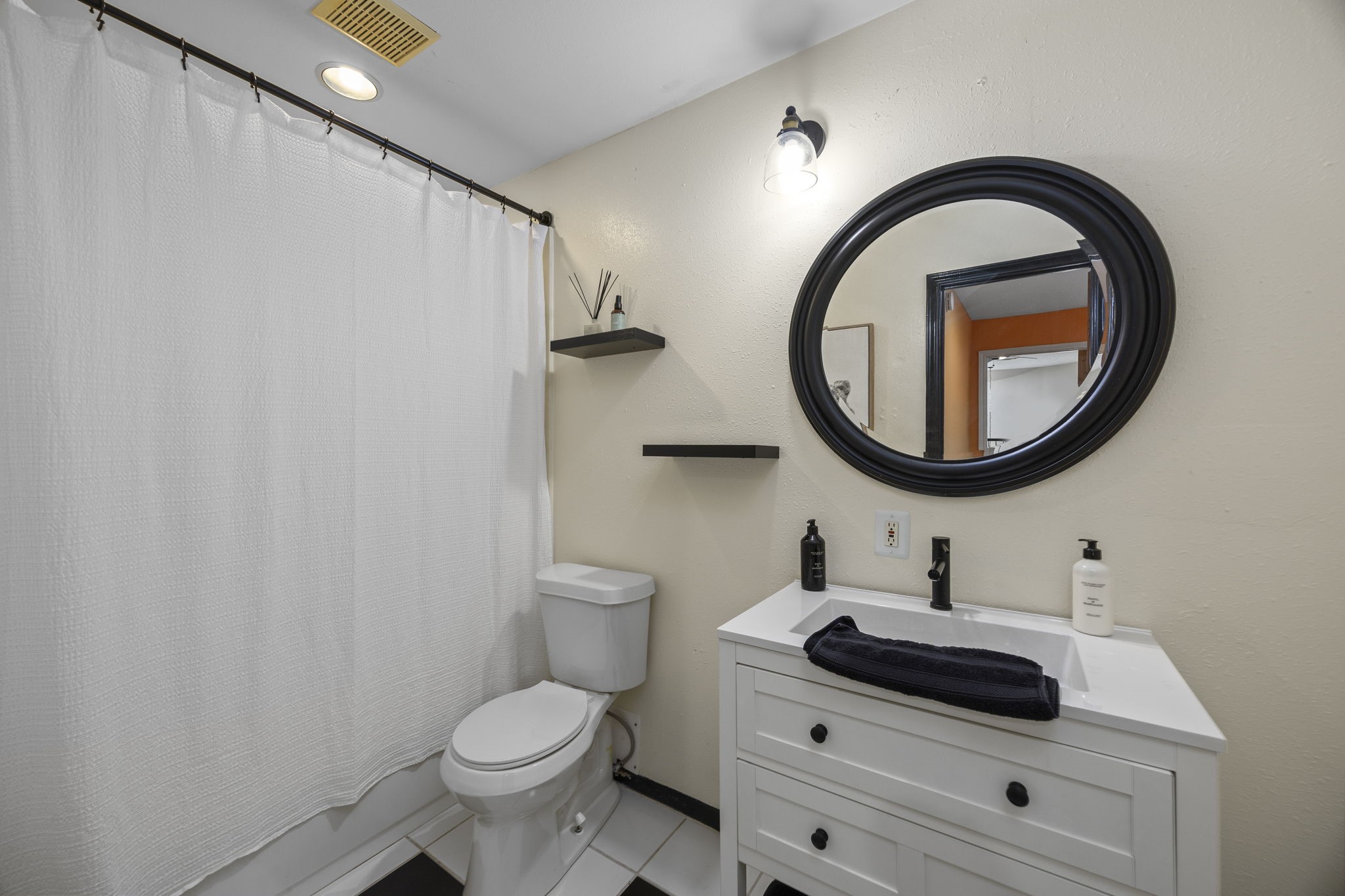 Private bathroom features a white vanity with storage, decorative round mirror, and tub/shower combination, completing this versatile upstairs suite.
