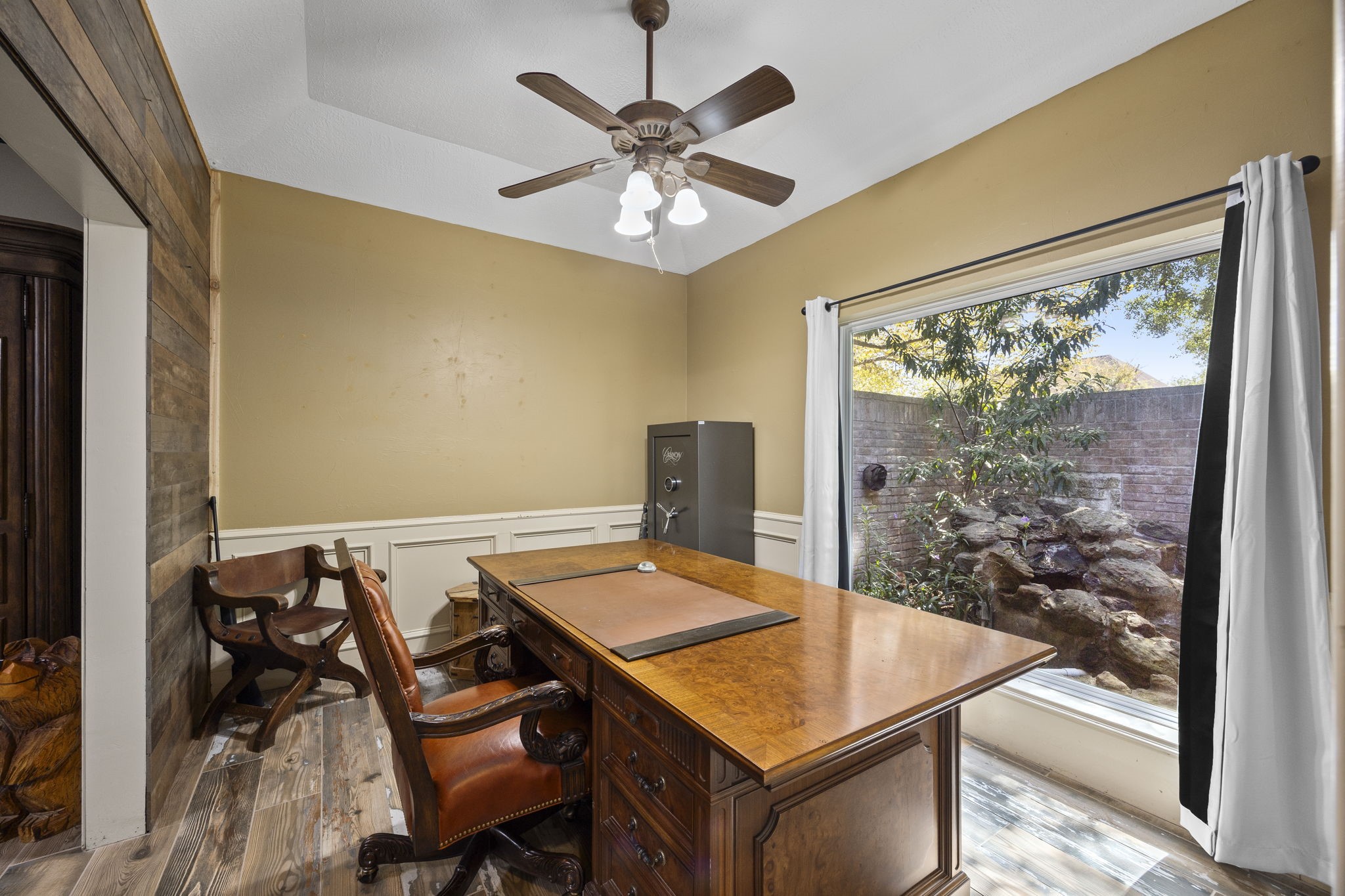 The private study features a vaulted ceiling, wood-look flooring, and a large picture window overlooking the landscaped front courtyard. A comfortable setting for working from home while enjoying views of the outdoors.