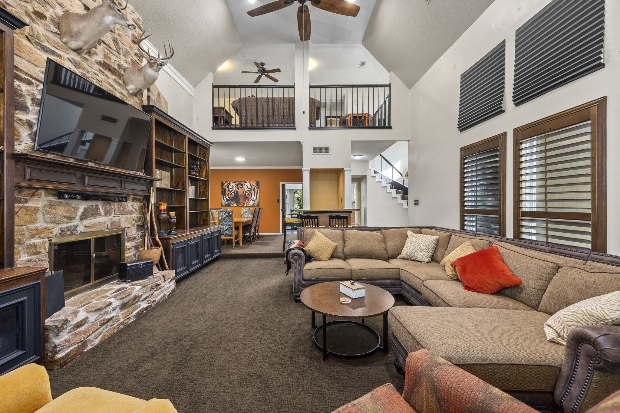 The dramatic two-story living room is anchored by a floor-to-ceiling stone fireplace flanked by extensive built-in cabinetry. Vaulted ceilings, an open upstairs balcony, and generous seating space create an impressive setting for gathering and entertaining.