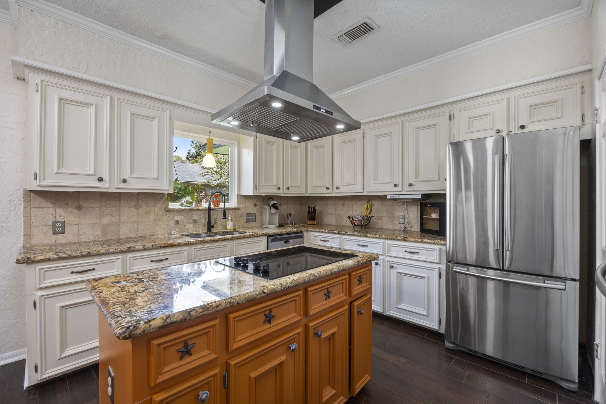 A window above the kitchen sink provides views outdoors, while generous counter space offers plenty of room for meal preparation. The combination of perimeter countertops and a central island creates multiple work areas, with abundant cabinetry for storage.