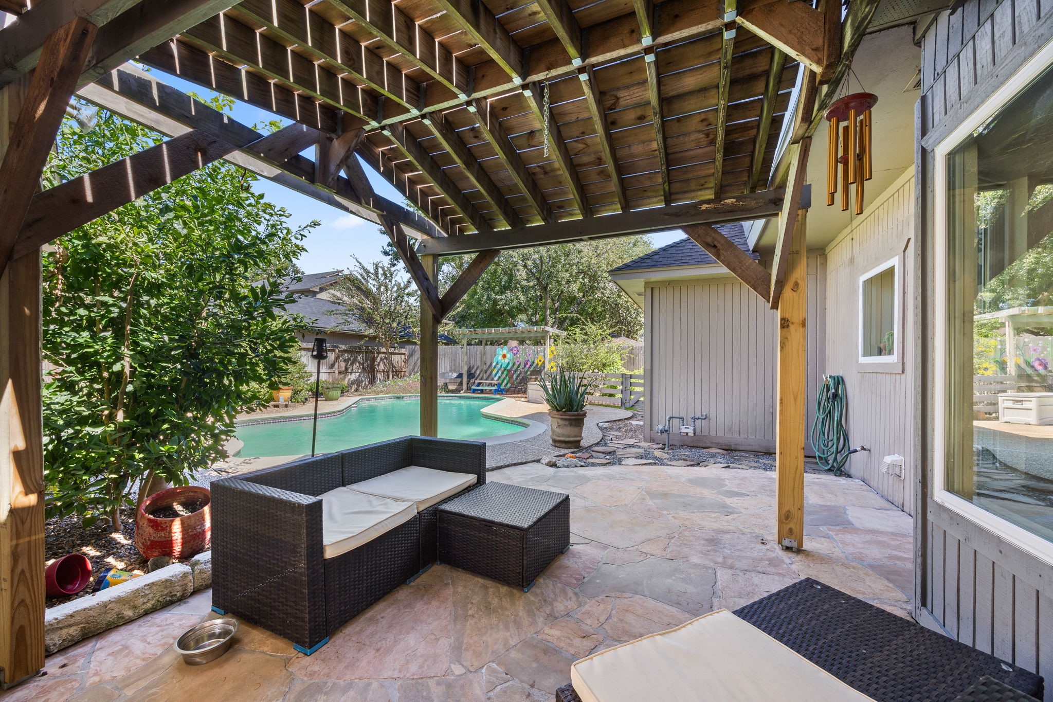 Spacious covered patio with wood-beamed structure offers a shaded retreat for outdoor seating, dining, and entertaining. Conveniently located alongside the pool, it provides an inviting space to relax and enjoy the backyard.