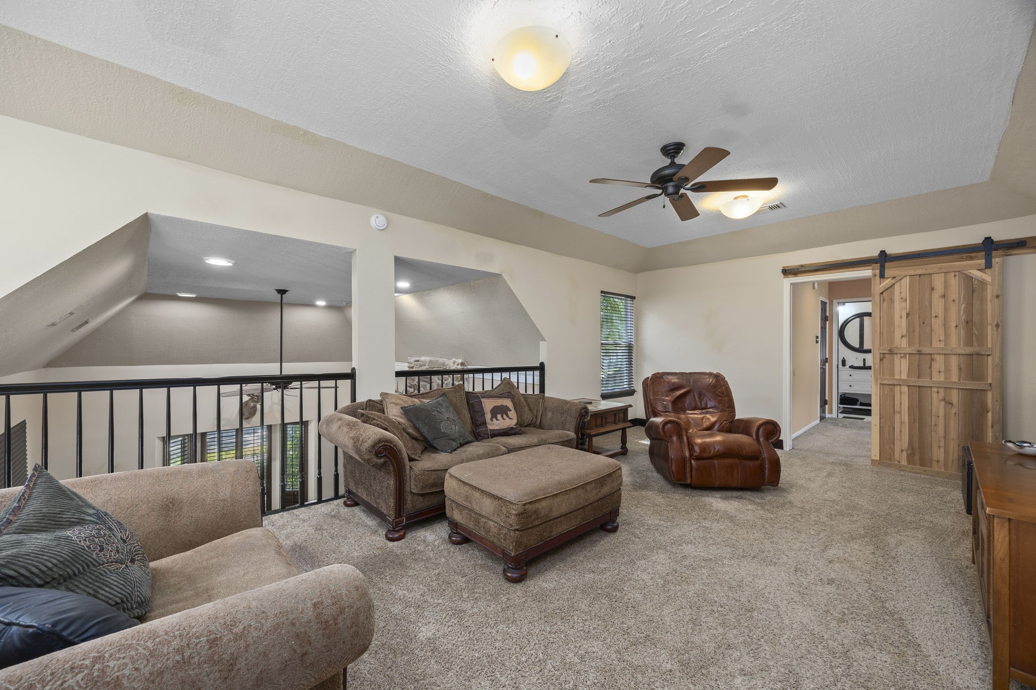Spacious upstairs game room overlooks the main living area below and offers plenty of room for comfortable seating, entertainment, and relaxation. A sliding barn door leads to an adjoining room.