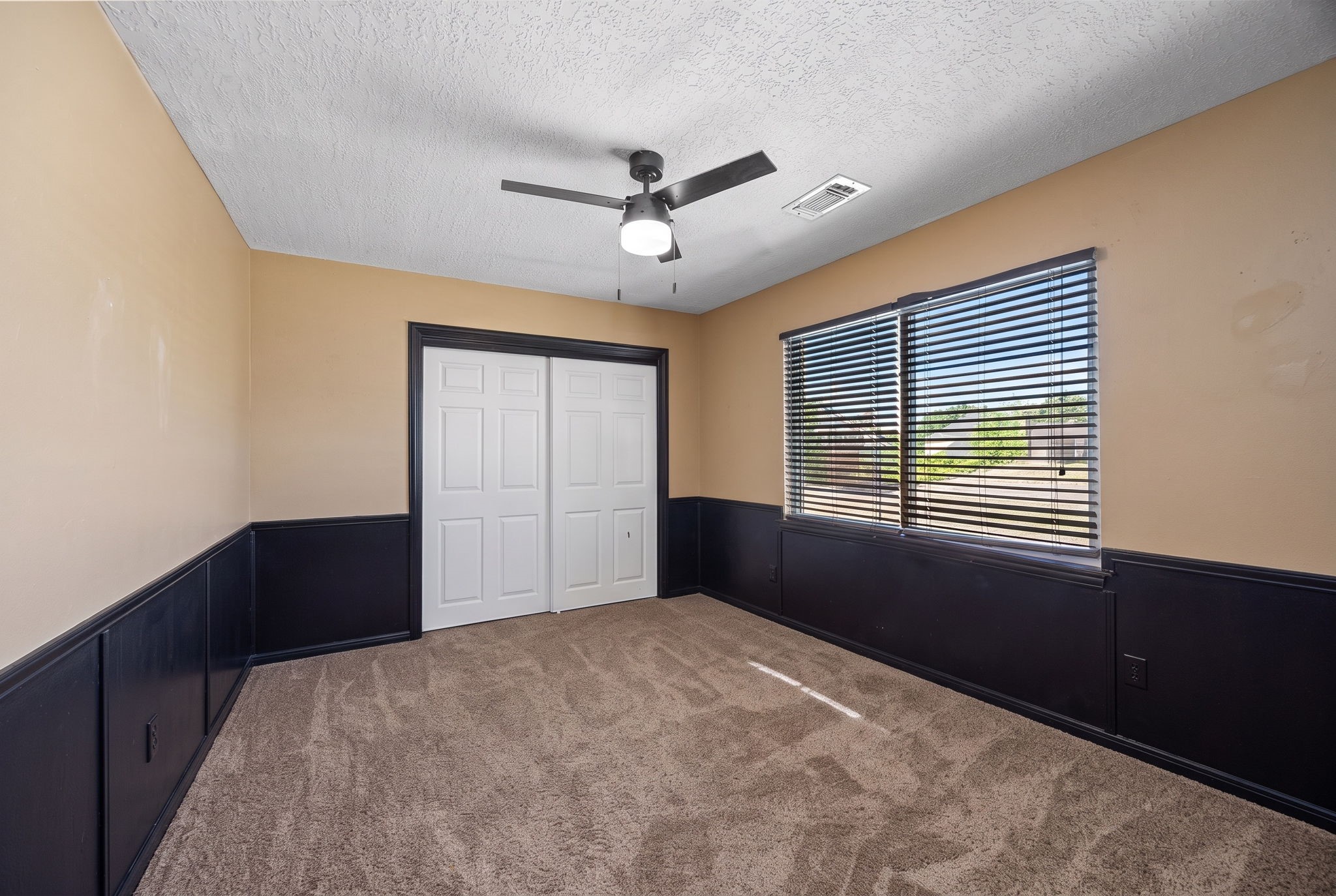 Another upstairs bedroom offers generous floor space, a ceiling fan, double-door closet, and contrasting dark wainscoting that adds character to the room.