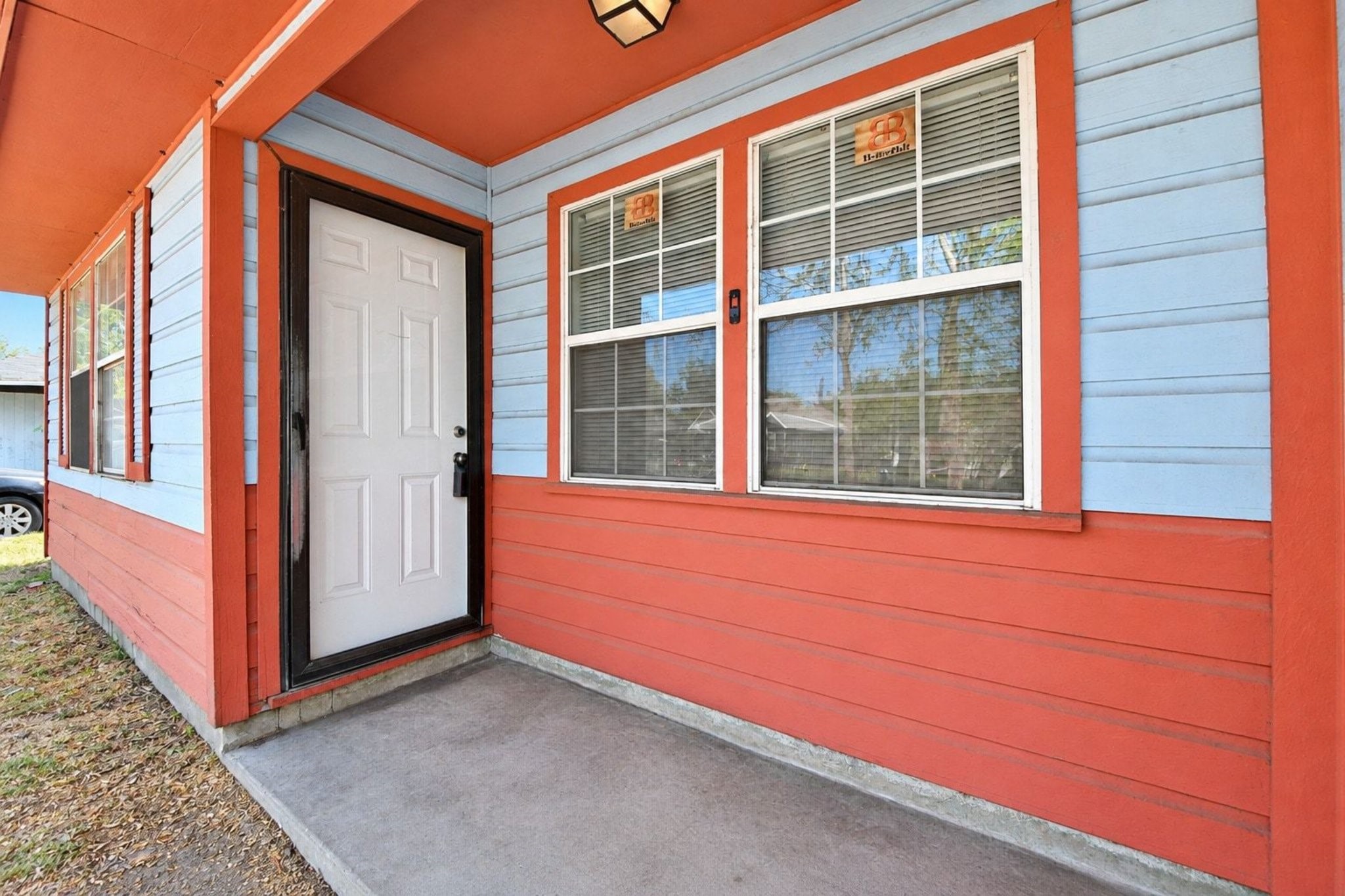 Front porch features a fresh orange exterior, white entry door, and large windows that bring in plenty of natural light.