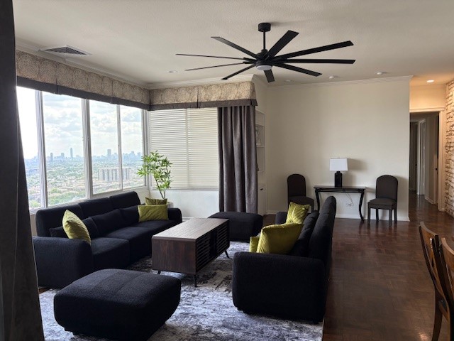 Spacious living room with modern furniture, large windows offering stunning city views, and a sleek ceiling fan.
